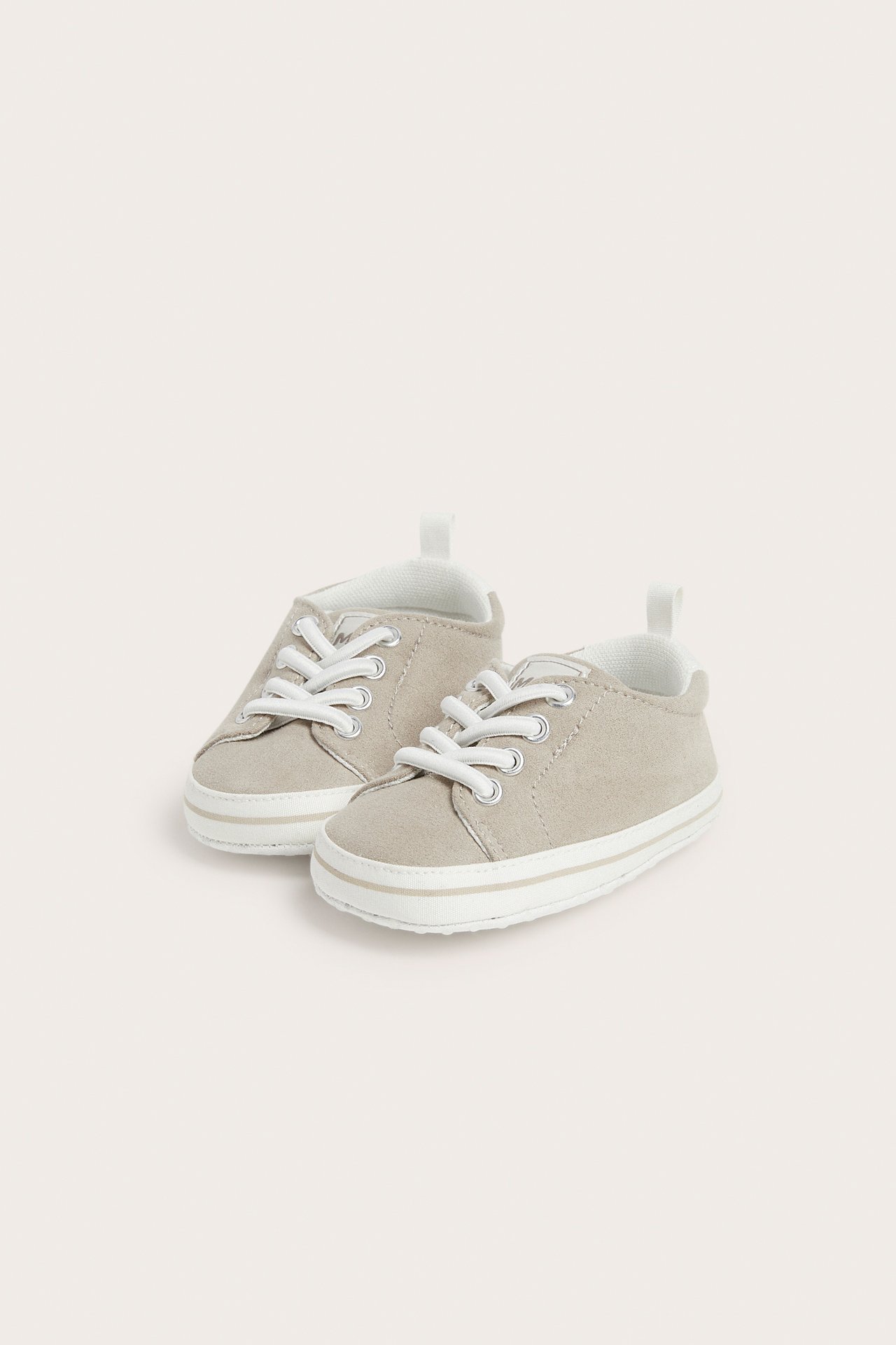 Forfra, myke beige babysneakers med hvite skolisser og antiskli-såler.