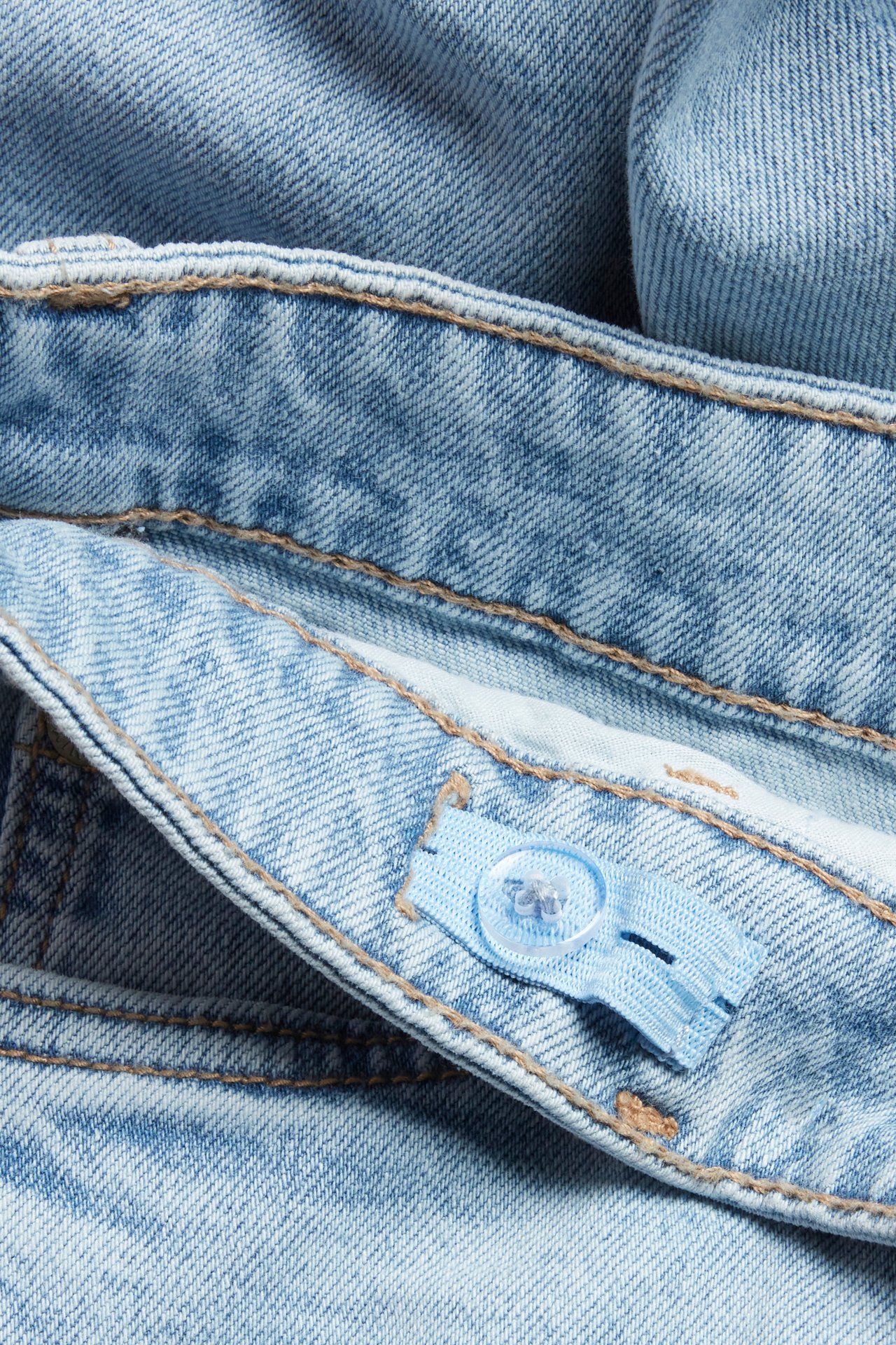 Zbliżenie na jasnoniebieskie proste dżinsy dziecięce, pokazujące regulowany elastyczny pas z przezroczystym guzikiem.