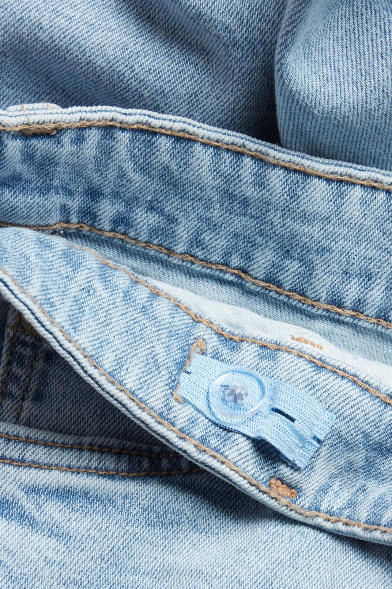 Zbliżenie na jasnoniebieskie proste dżinsy dziecięce, pokazujące regulowany elastyczny pas z przezroczystym guzikiem.