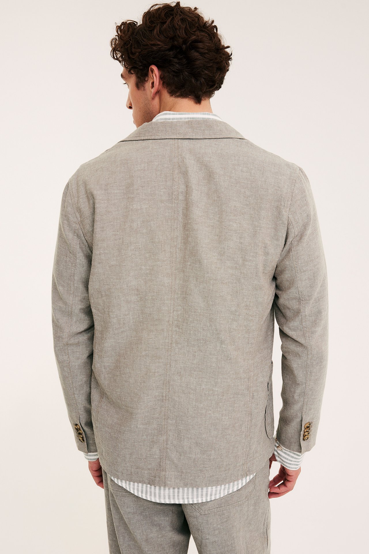 Mężczyzna od tyłu: jasnobrązowa marynarka regular fit z lnu, koszula w paski, spodnie.