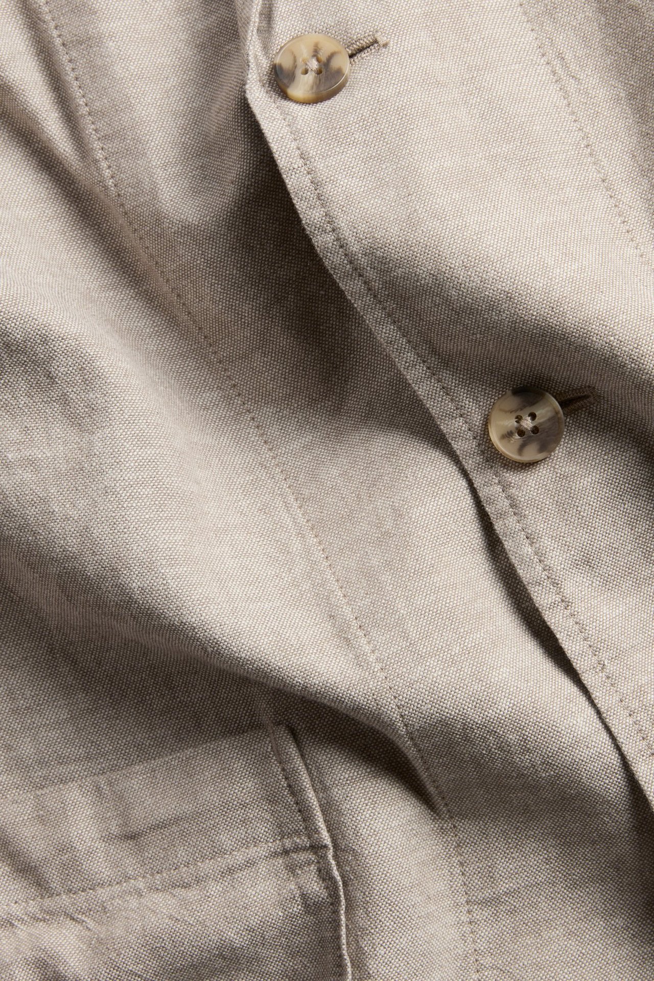Zbliżenie beżowej męskiej marynarki o regularnym kroju z mieszanki lnu z marmurkowymi guzikami.