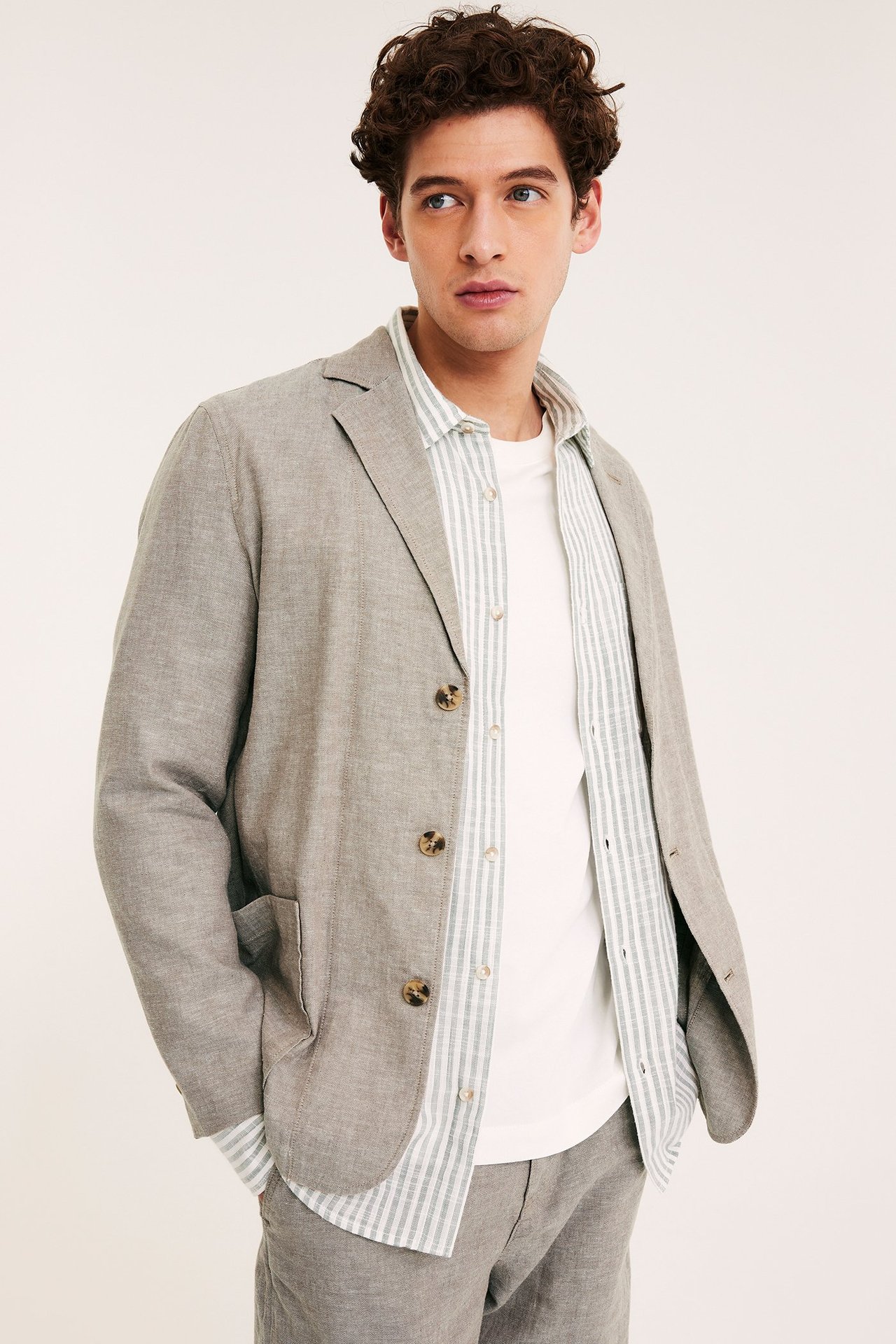 Frontvisning: Mann i brun regular fit linblanding blazer over stripete skjorte og hvit t-skjorte.