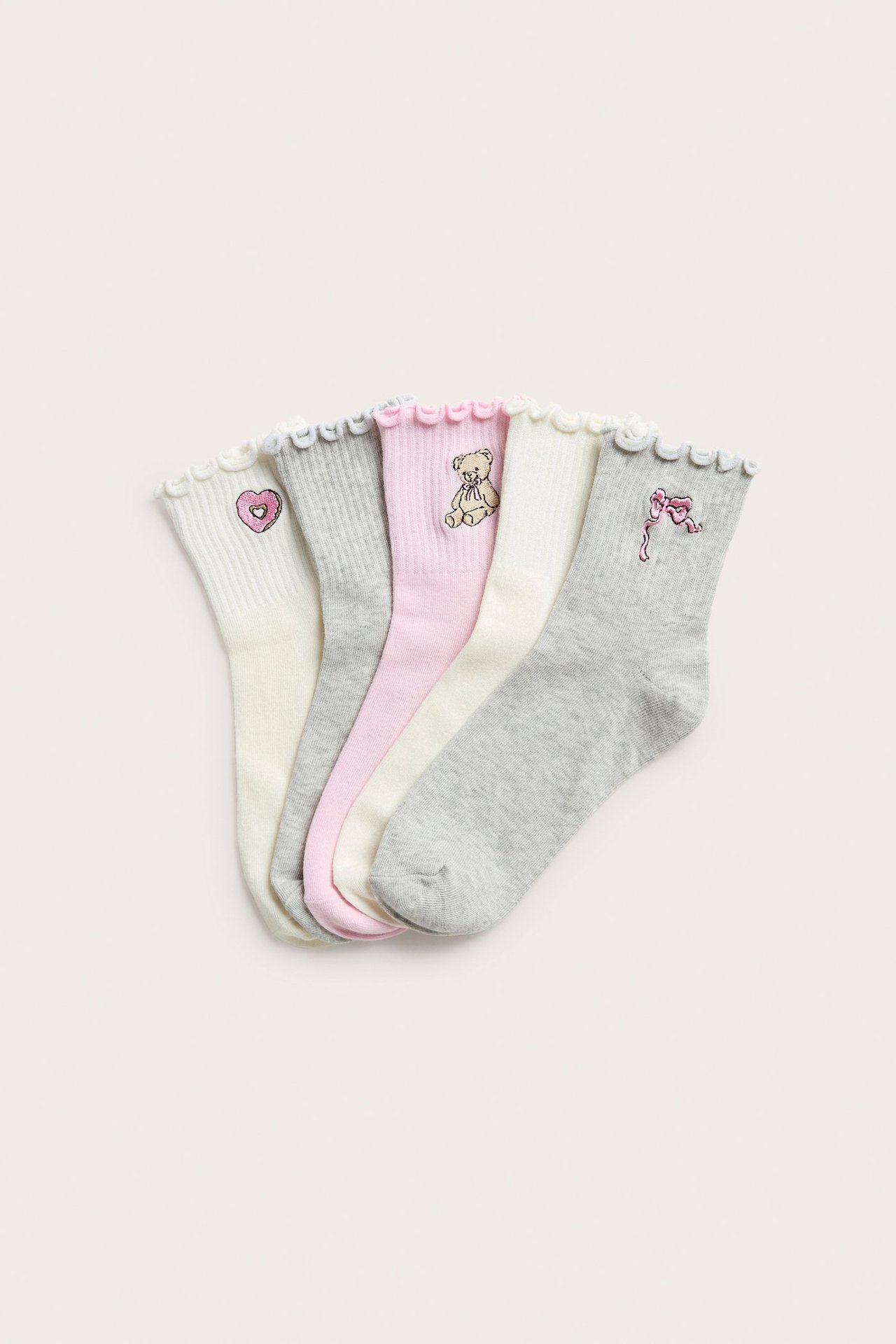 Överifrån, fem barnstrumpor i ljusgrått, vitt och rosa, med volangkanter och blandade tryck.