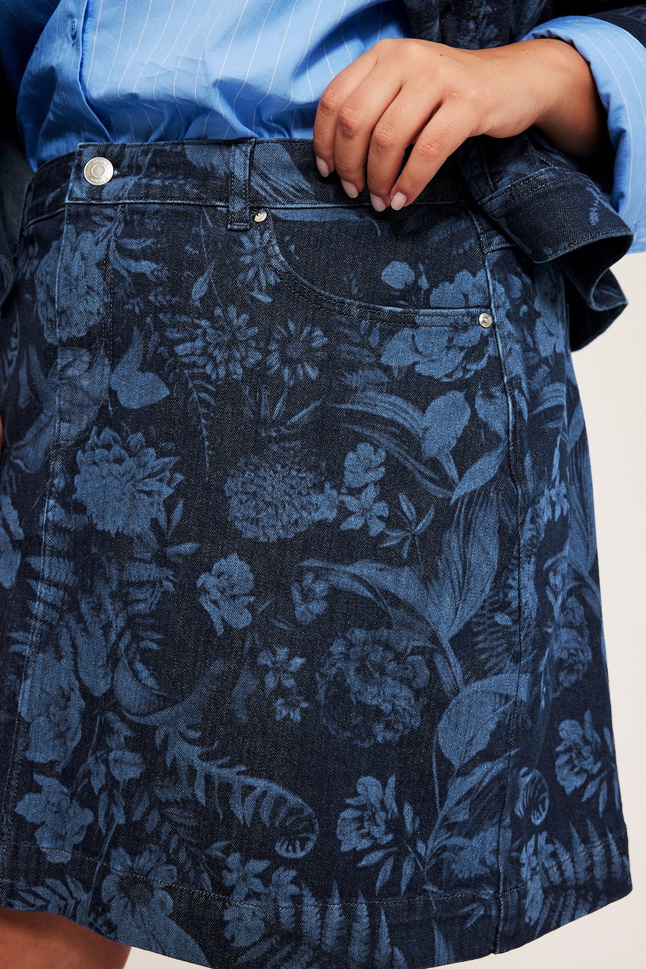 Lähikuva edestä naisesta tummansinisessä kukallisessa farkkuhameessa ja vaaleansinisessä raidallisessa paidassa.