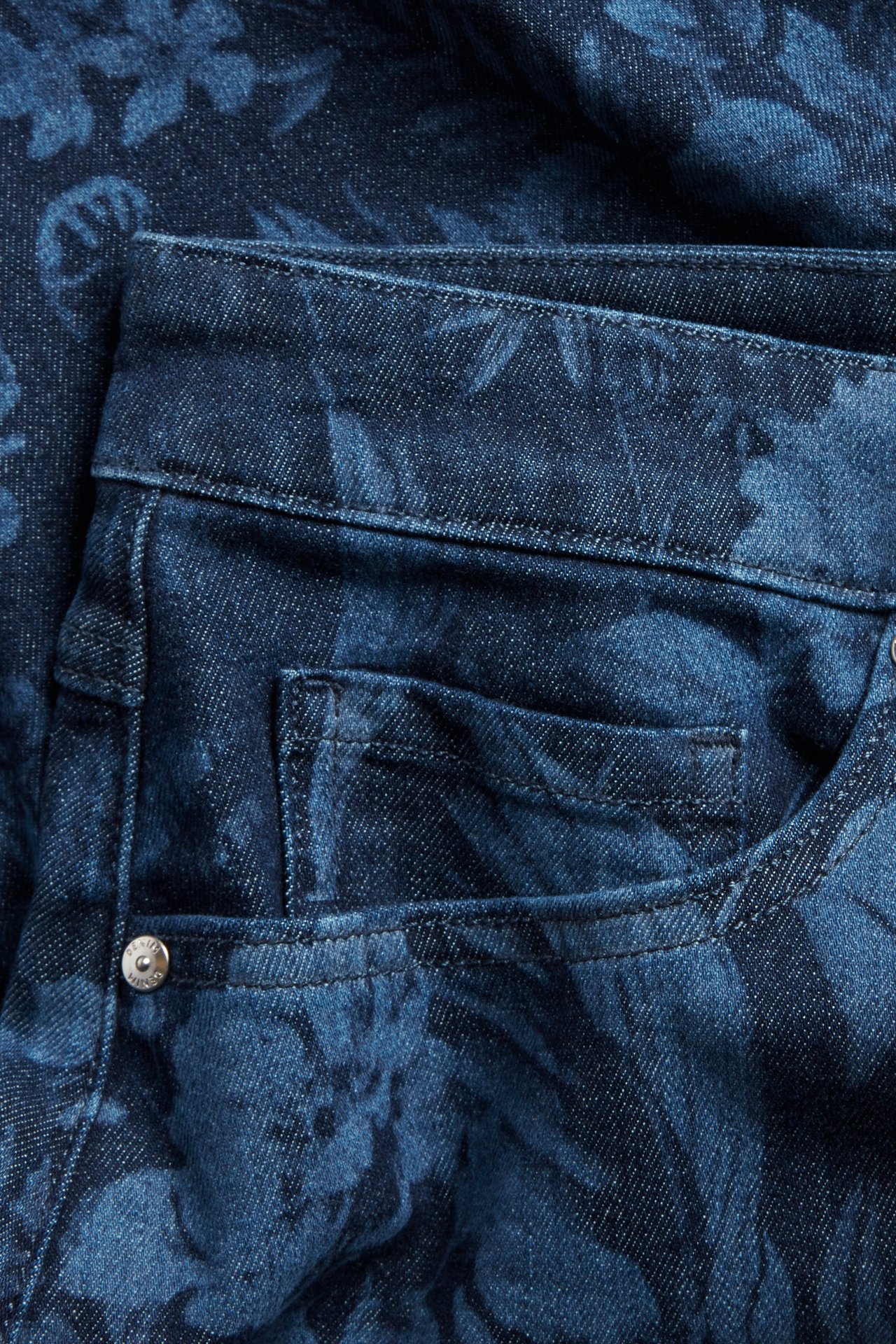 Närbild av en blå jeanskjol med lasertryckt blommönster, med en synlig framficka.