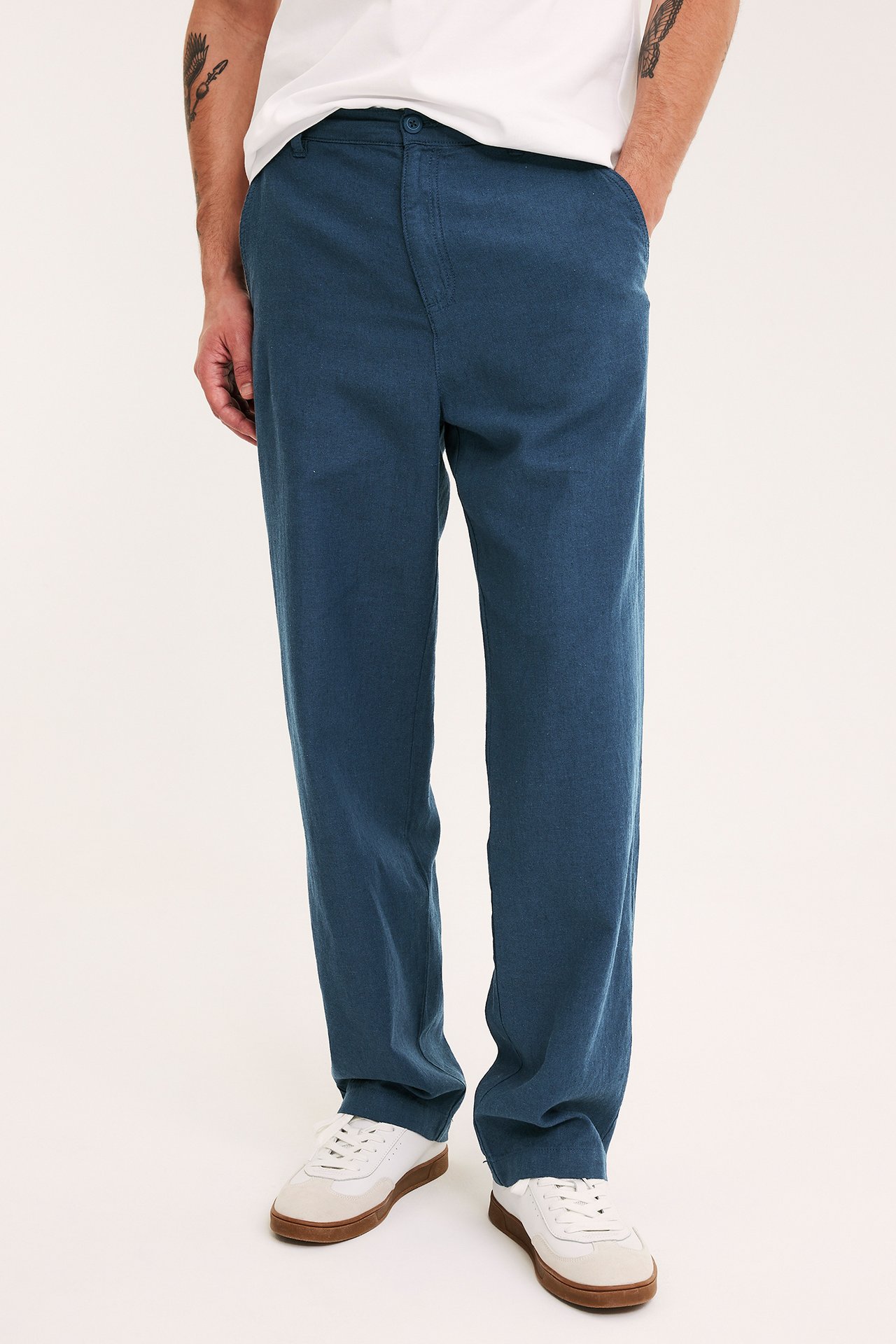 Mężczyzna w niebieskich lnianych spodniach, białym T-shircie i białych tenisówkach.