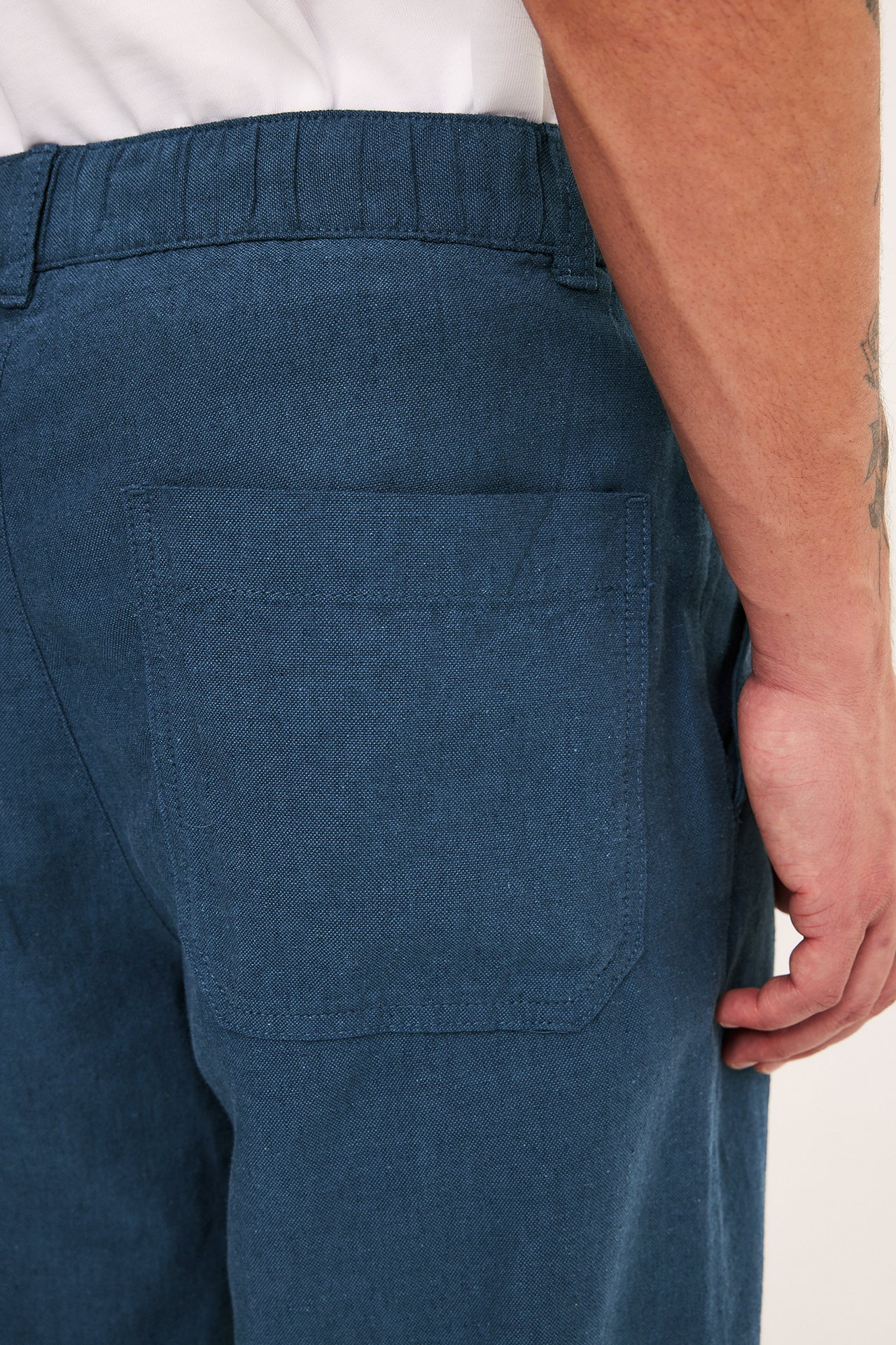 Widok z tyłu: Mężczyzna w niebieskich spodniach z mieszanki lnu o regularnym kroju, z gumką w pasie i tylną kieszenią.