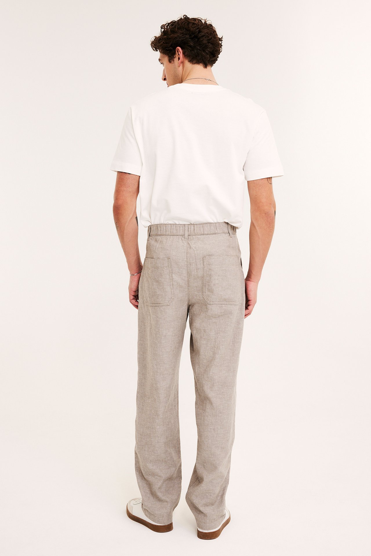 Takakuva: Mies yllään vaaleanruskeat, suorat pellavasekoitehousut joustovyötäröllä ja valkoinen t-paita.