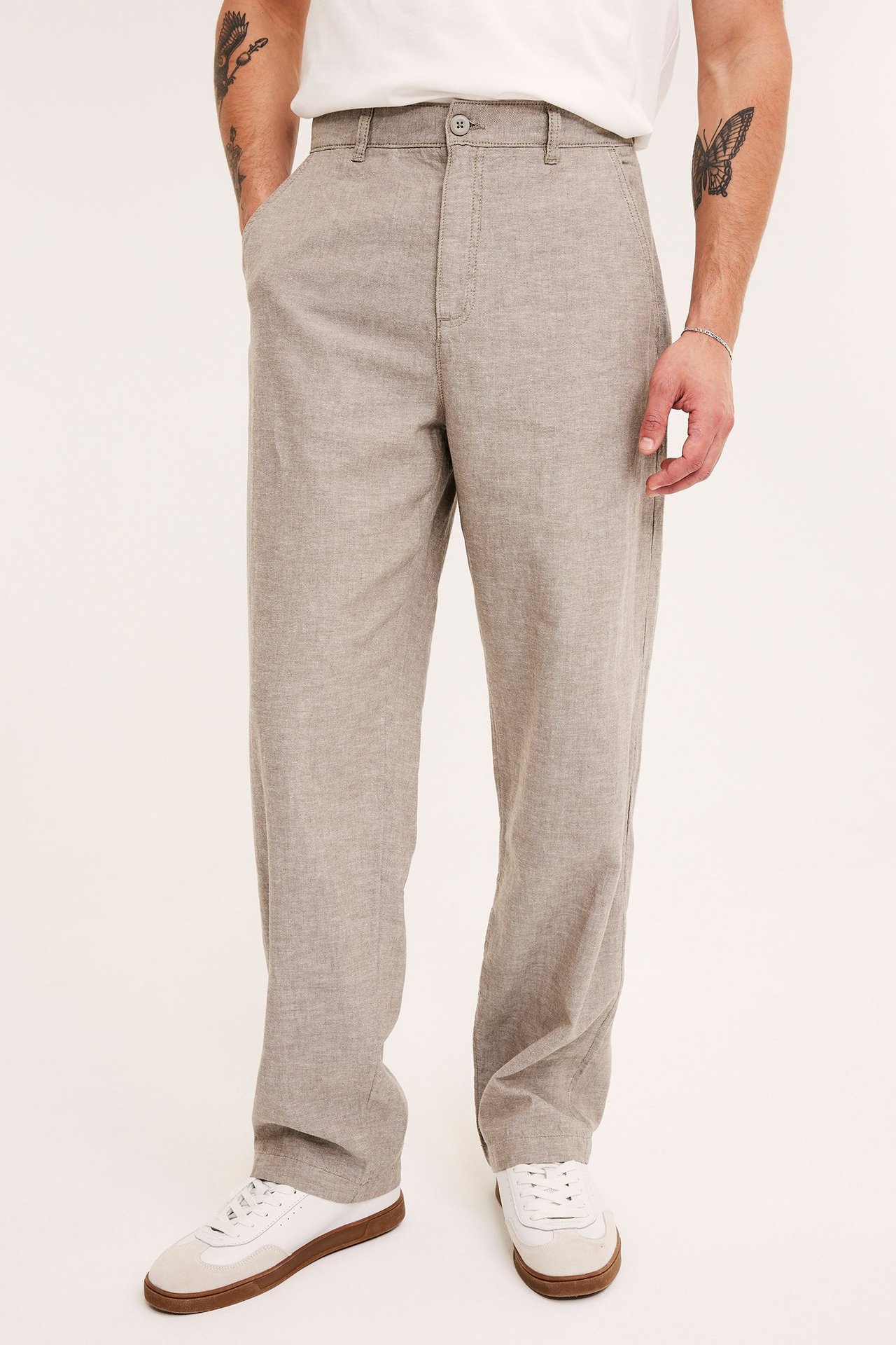 Widok z przodu: mężczyzna w jasnobrązowych spodniach z lnu, białym T-shircie i białych tenisówkach.