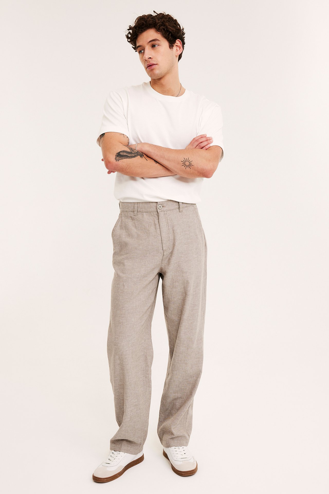 Man framifrån i ljusbruna regular fit linnemixbyxor, vit t-shirt och vita sneakers.