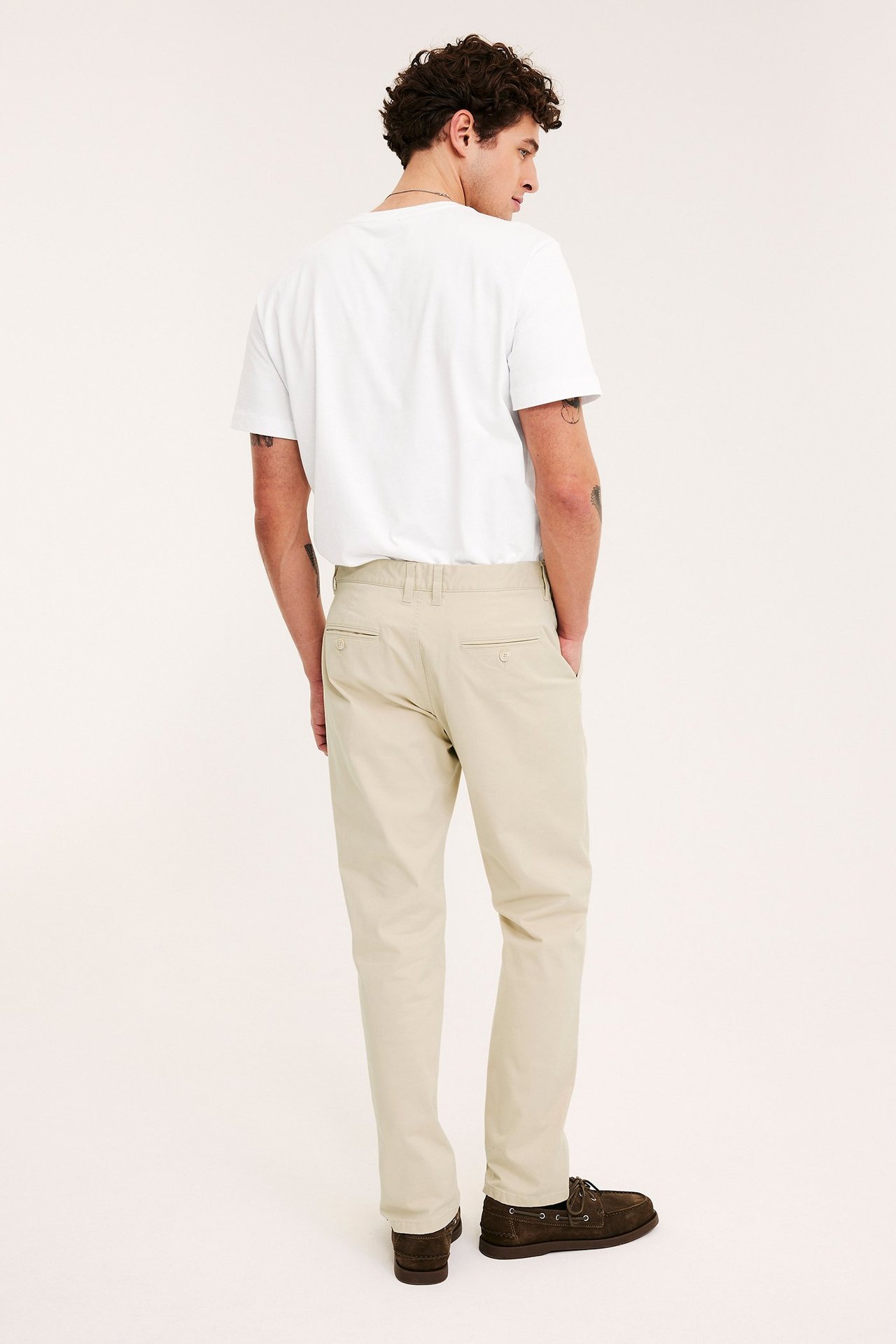 Mann bakfra i beige regular fit chinos, hvit t-skjorte og brune seilersko.