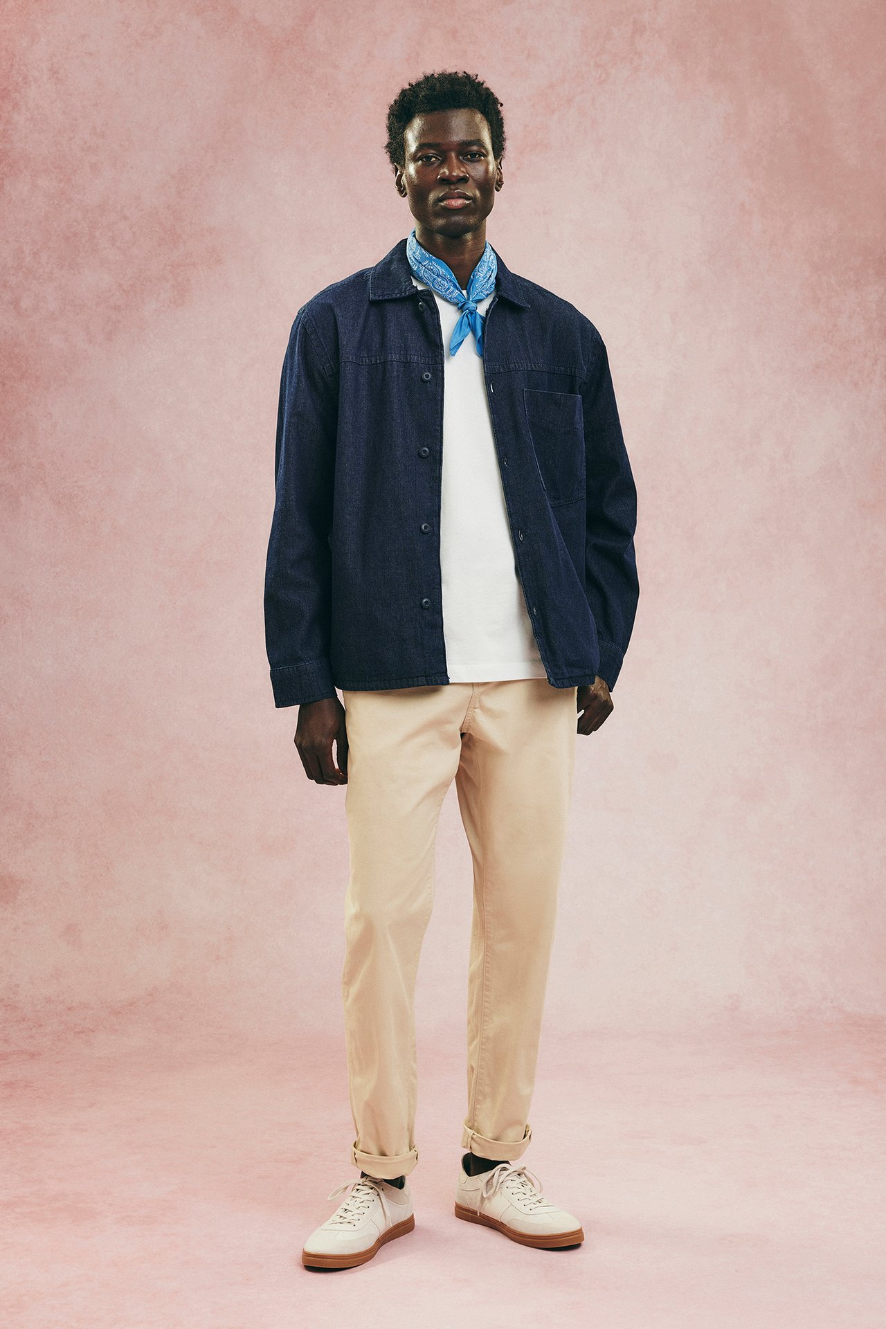 Framifrån: Man i beige regular fit bomullschinos, mörkblå skjorta, vit t-shirt, blå bandana, vita sneakers.