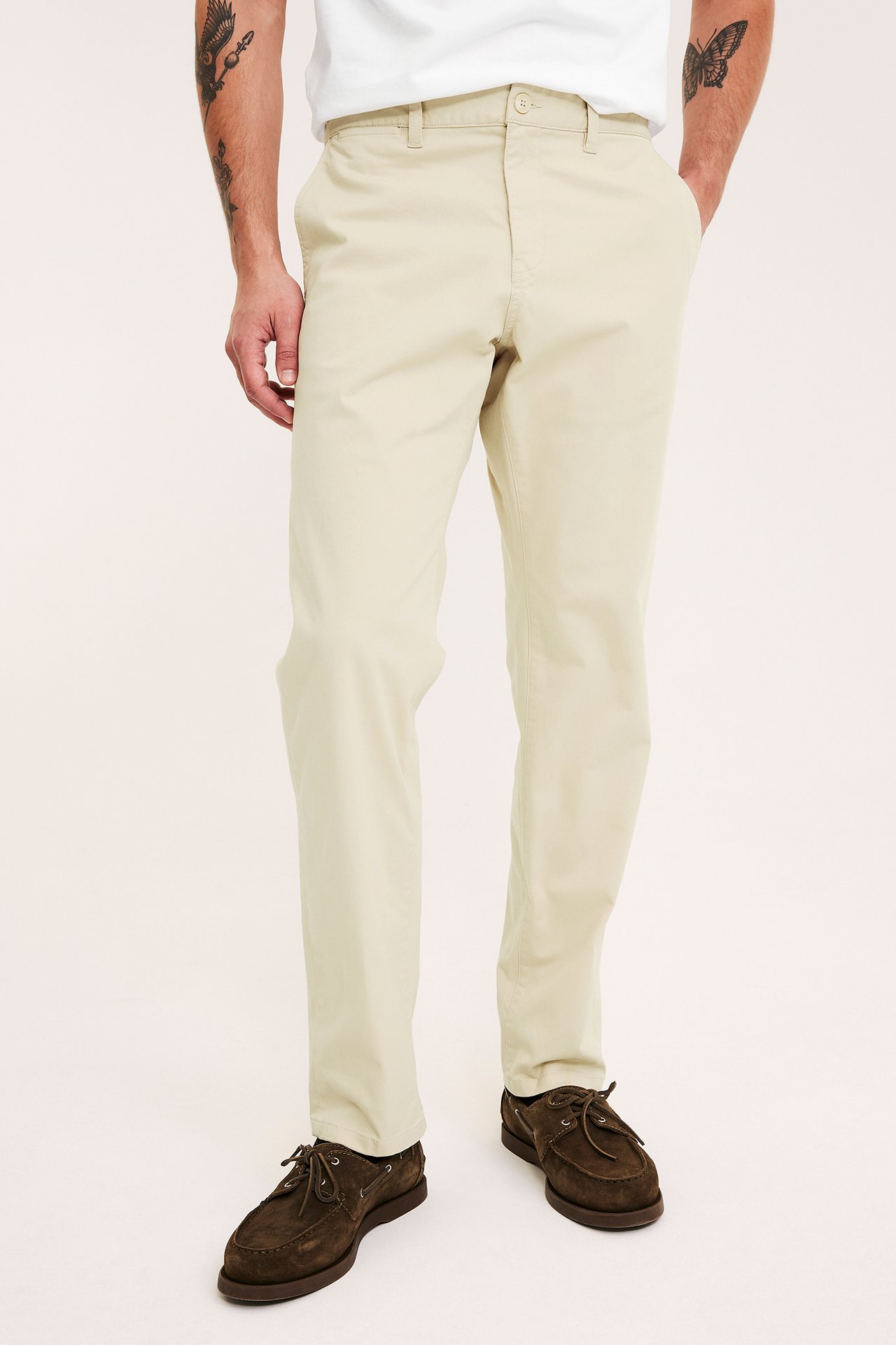 Frontvy av en mann i beige regular fit chinos, en hvit t-skjorte og mørkebrune båtsko.