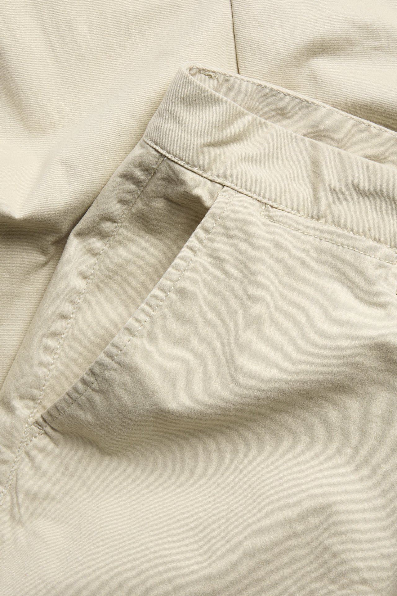 Närbild på beiga regular fit chinos i bomullsmix för herr, visar midja och sidoficka.