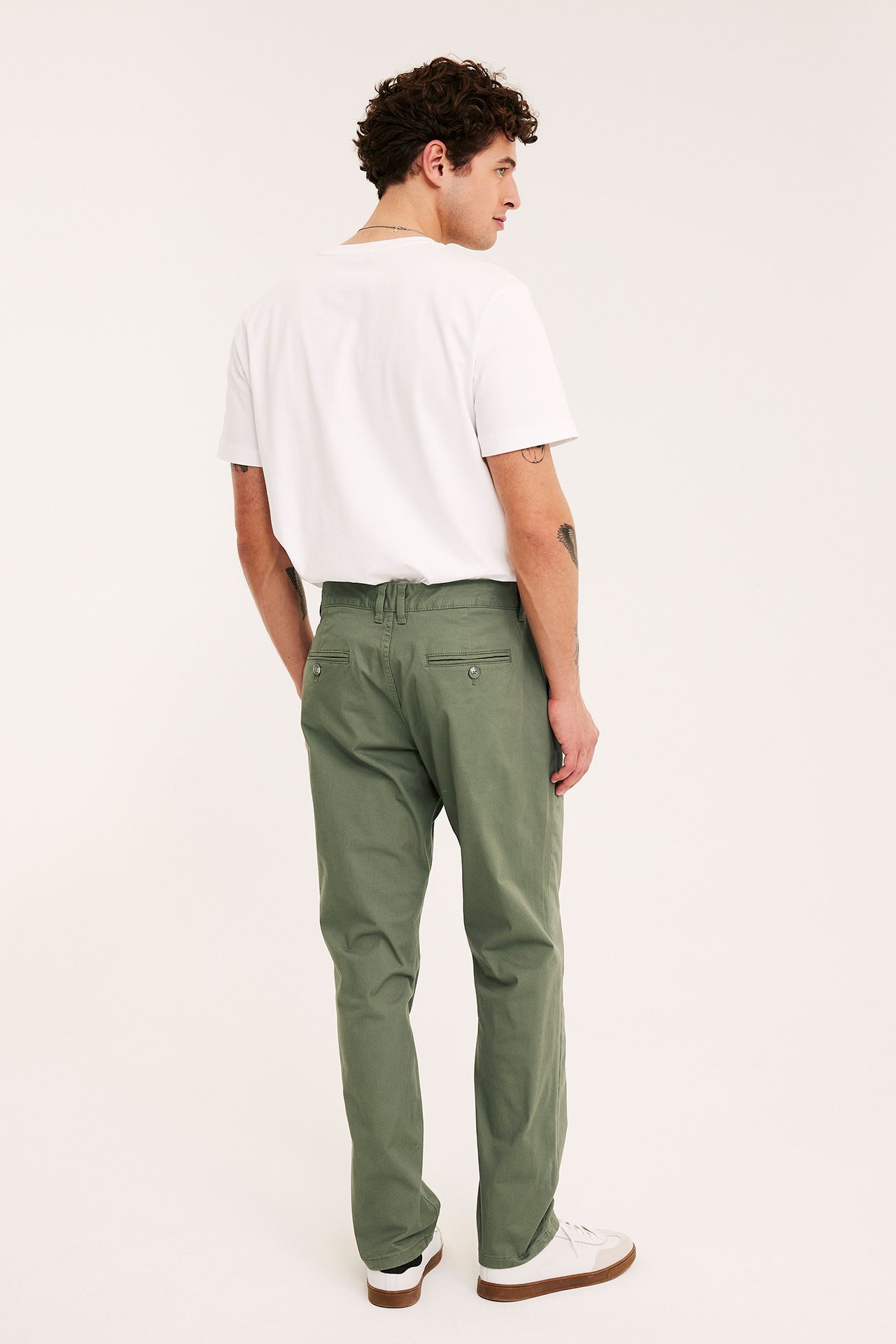 Bakfra: mann i mørkegrønne regular fit bomullschinos, hvit t-skjorte og hvite joggesko.