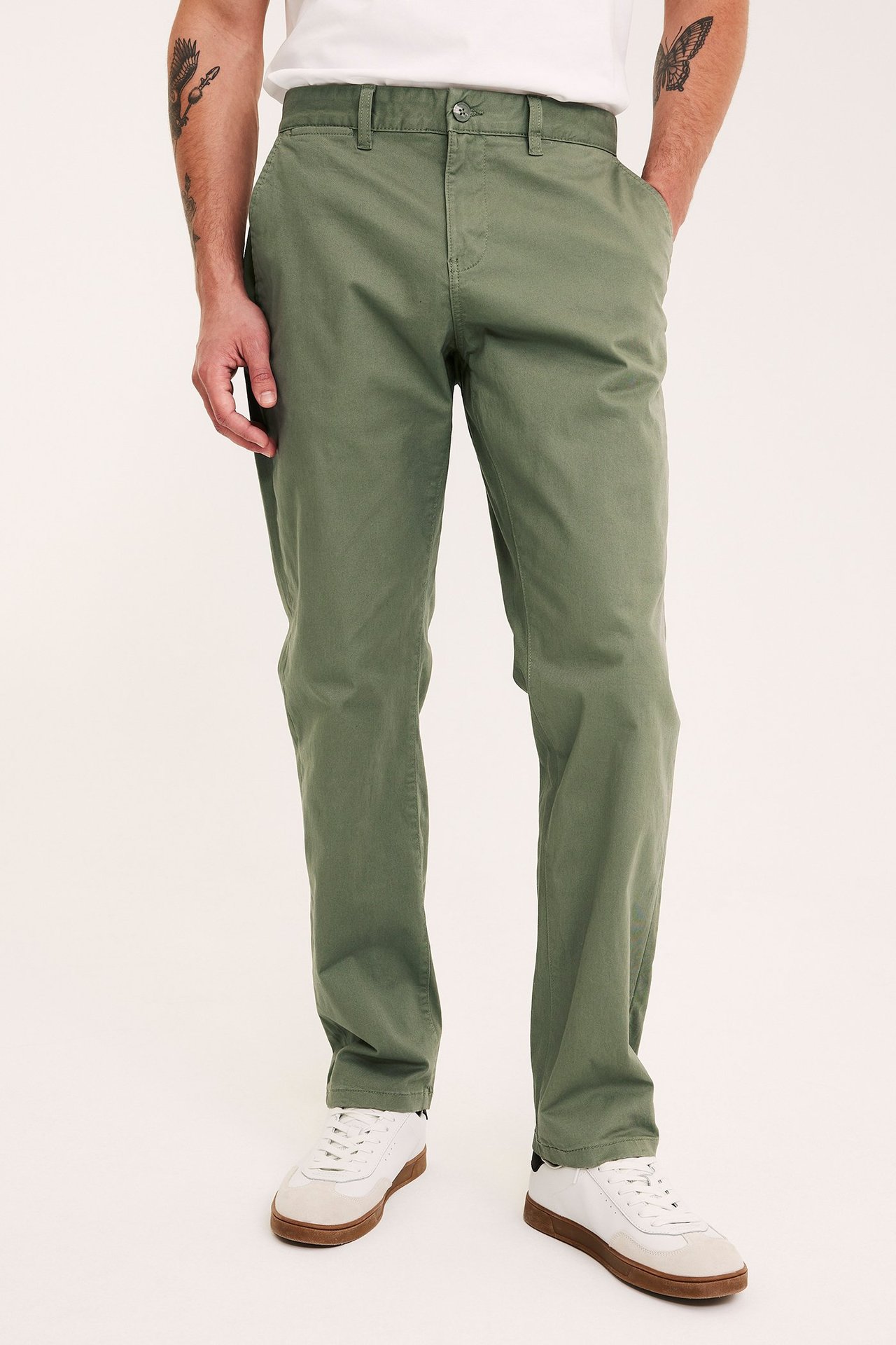 Frontbilde av en mann i mørkegrønne regular fit chinos i bomullstwill, en hvit t-skjorte og hvite joggesko.