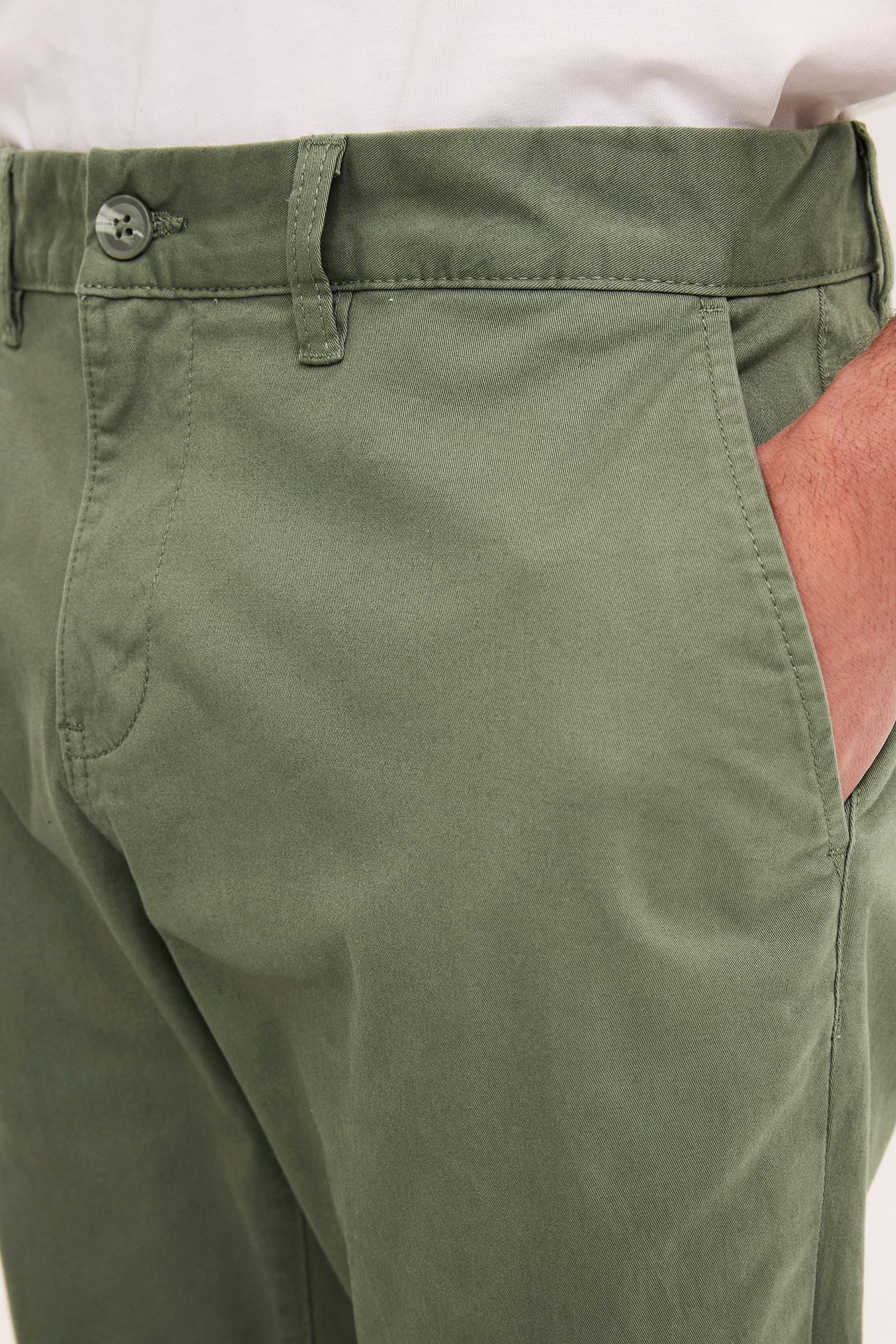 Nærbilde forfra av mørkegrønne regular fit chinos i bomullstwill med en hånd i lommen.