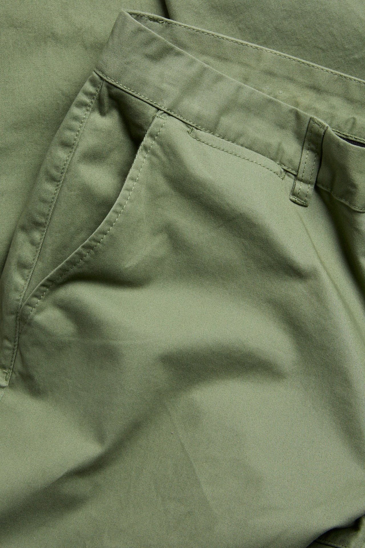 Närbild på mörkgröna regular fit bomull-elastan chinos för män, visar en framficka och linning.