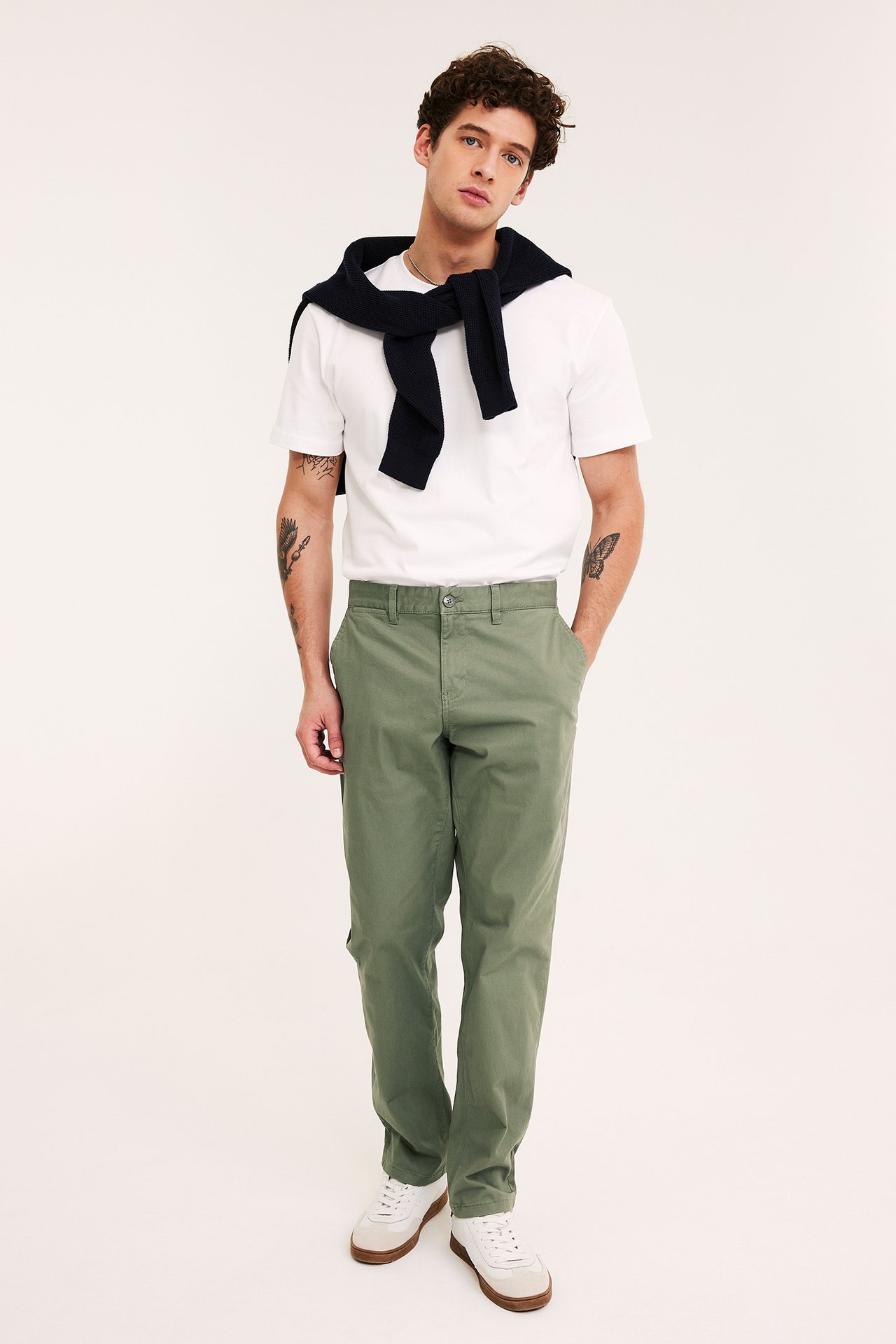 Frontvisning: Mann i mørkegrønne regular fit chinos, hvit t-skjorte og marineblå genser.