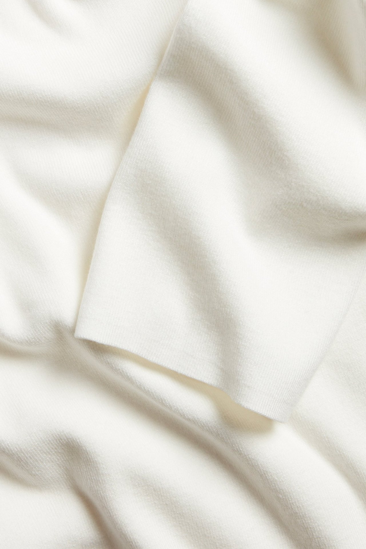Zbliżenie miękkiej, écru dzianiny swetrowej, ukazujące subtelną fakturę i fałdy materiału.