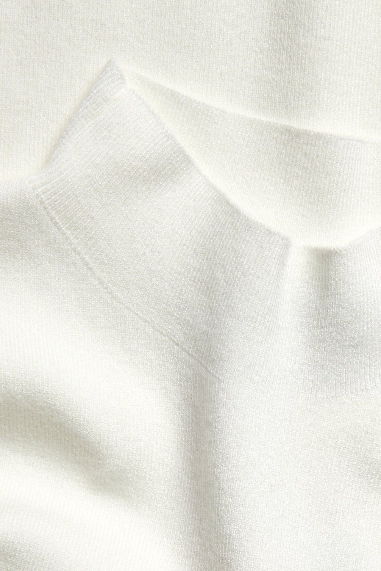 Nærbilde av en offwhite strikkevest med krage og fin strikket tekstur.