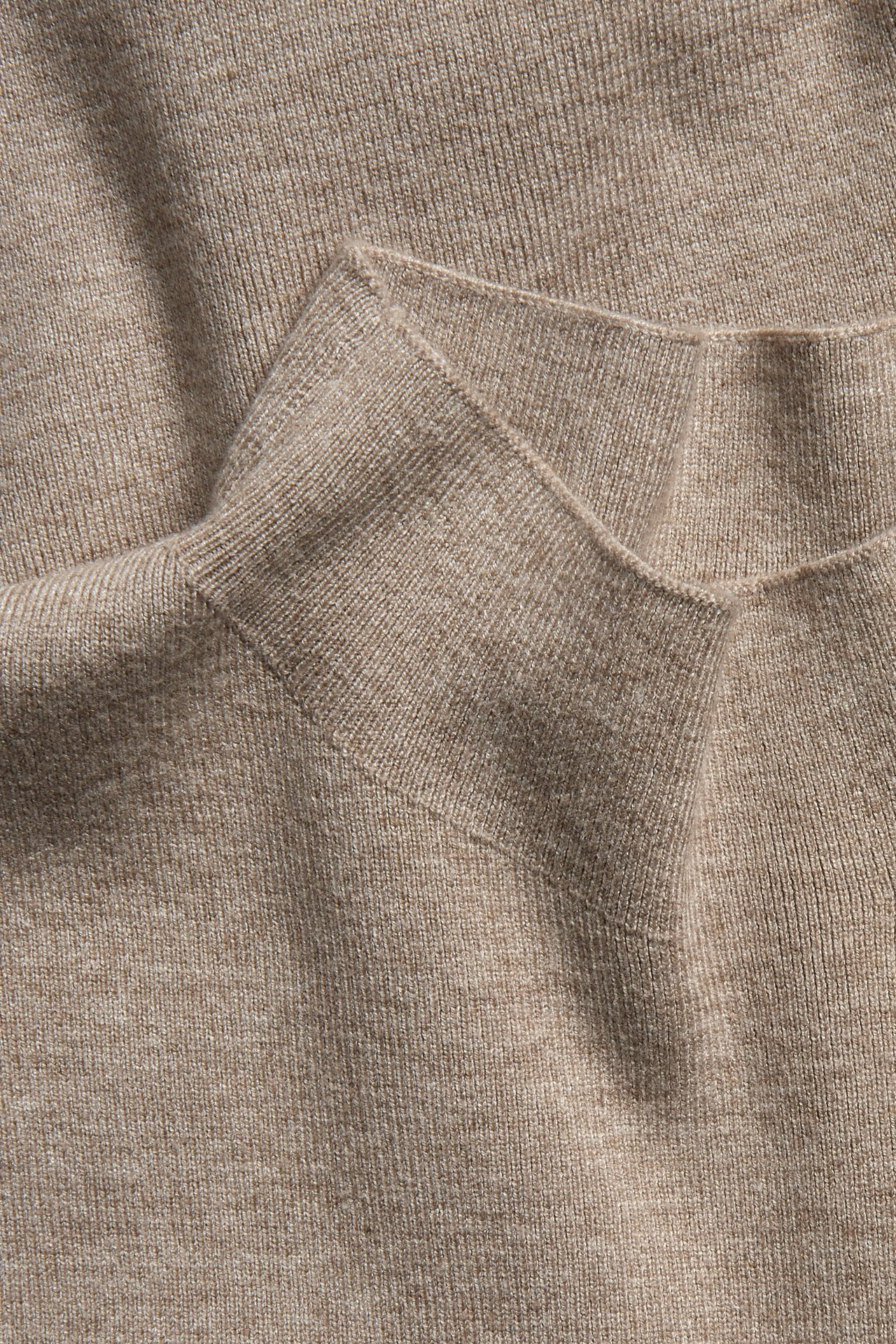 Zbliżenie beżowej melanżowej dzianinowej kamizelki z prążkowanym kołnierzem.