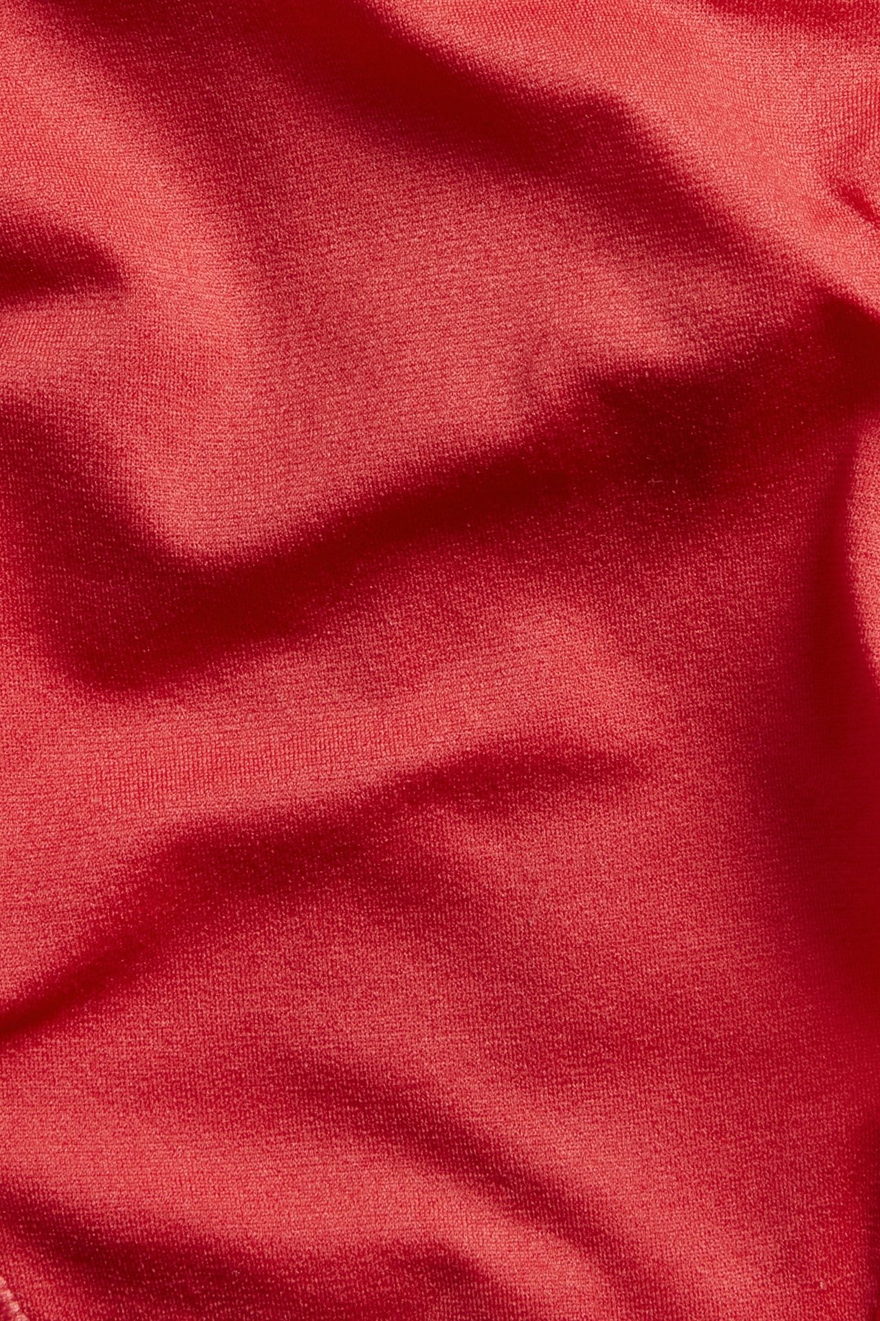 Nærbilde av røde stringtruser, viser det myke, tynne, elastiske ensfargede røde stoffet med folder.