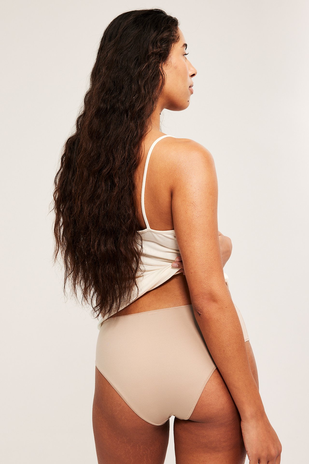 Widok z boku tyłu kobiety w jednobarwnych brązowych figach brazylijskich i jasnym topie.