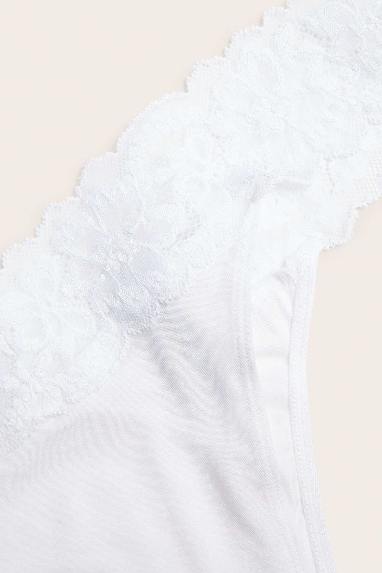 Lähikuva valkoisista lyocell-stringeistä, joissa on pehmeä pitsireuna vyötäröllä.