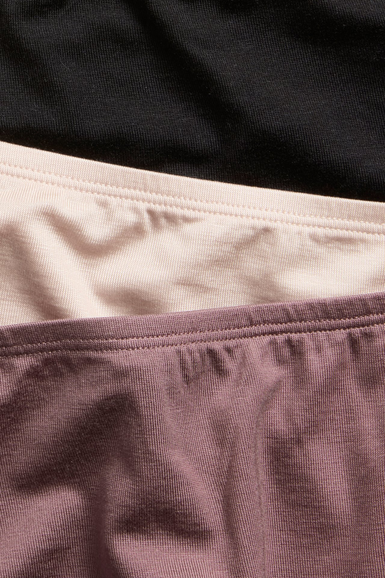Lähikuva kolmesta yksivärisestä lyocell-hipster-alushoususta mustana, vaaleanpunaisena ja tummanpunaisena.