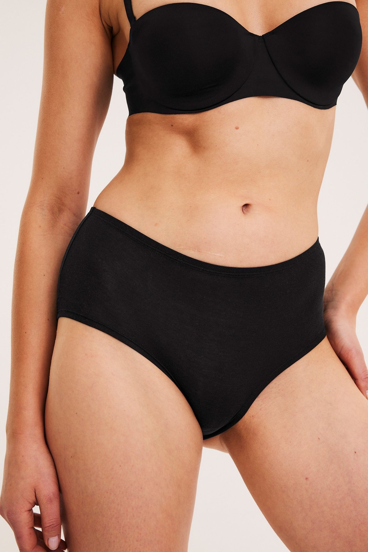 Naisen etukuva mustissa lyocell-hipster-alushousuissa ja mustissa olkaimettomissa rintaliiveissä.