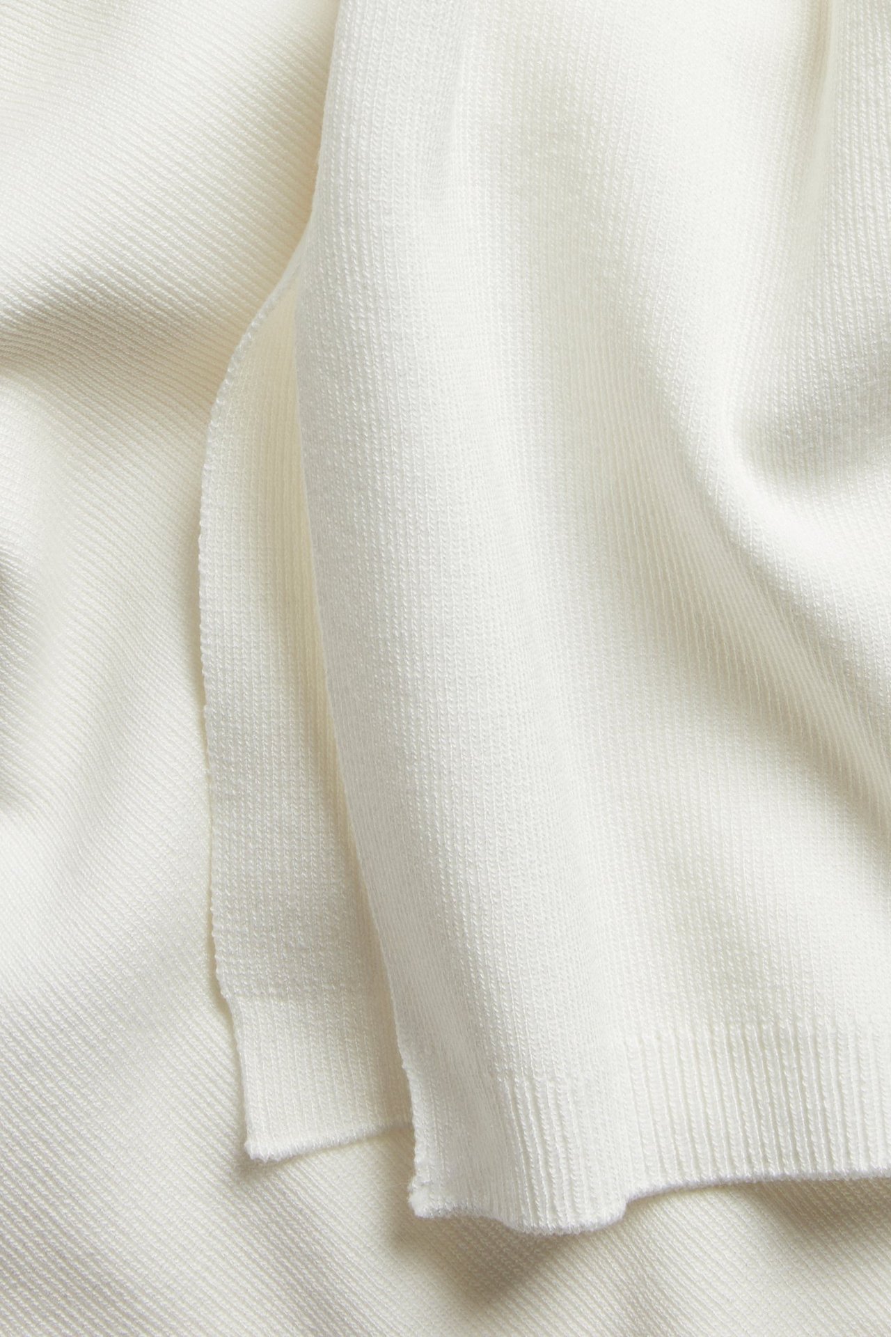 Lähikuva luonnonvalkoisesta hienoneulotusta lyhythihaisesta neuleesta, näyttäen sen sileän kankaan.