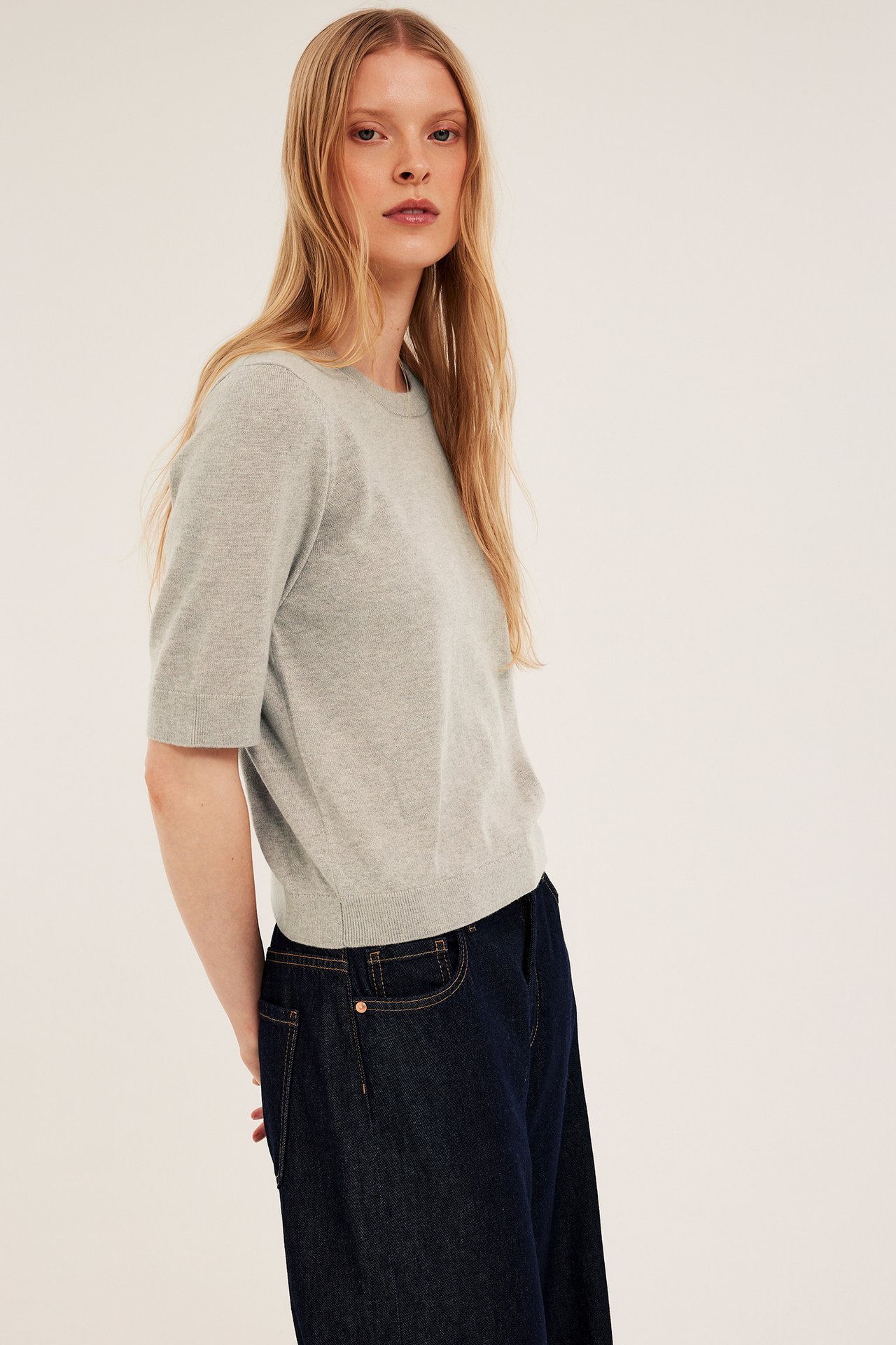 Nainen edestä: vaaleanbeigensävyinen meleerattu lyhythihainen villasekoitepusero ja tummansiniset farkut.