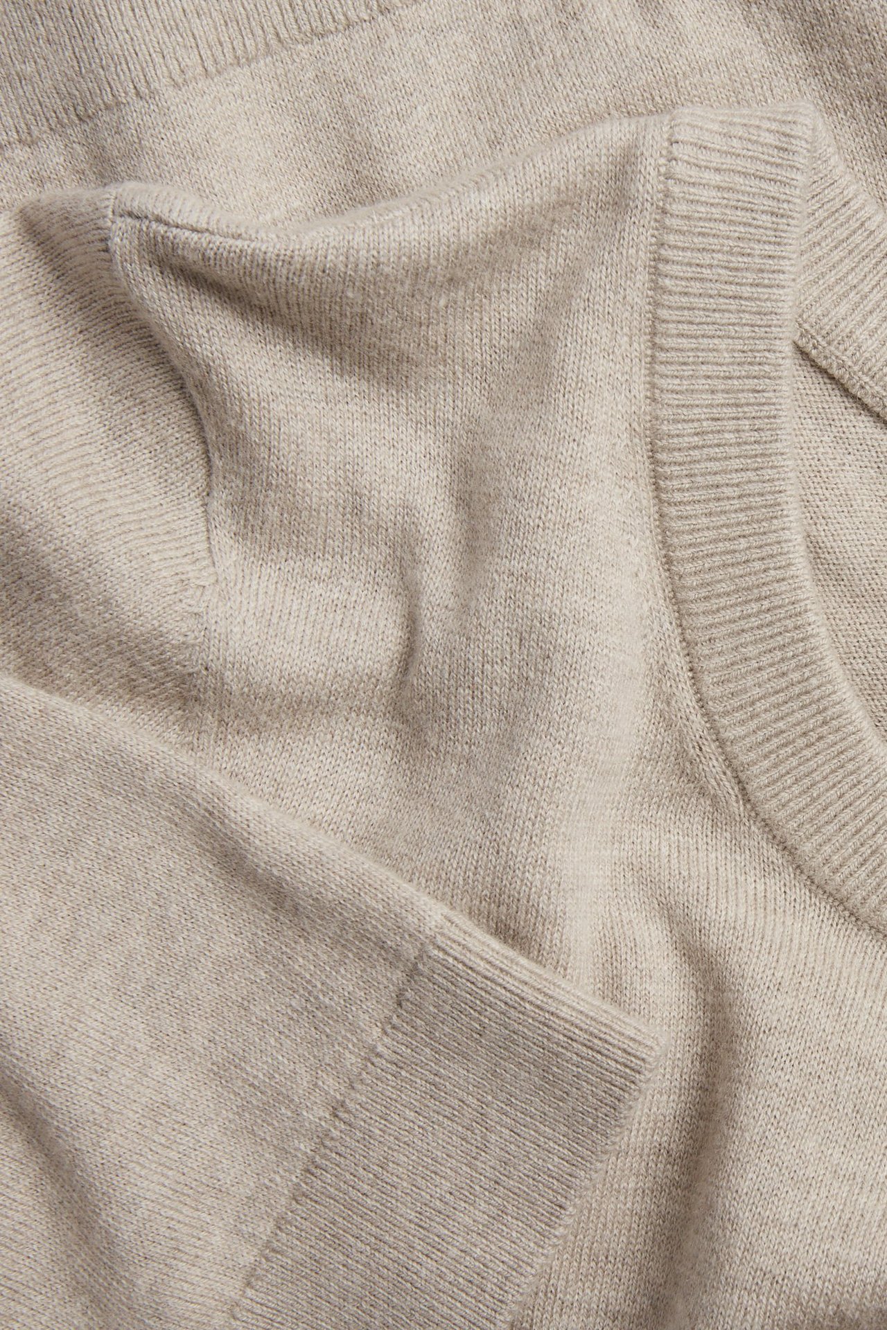 Zbliżenie na jasnobeżowy melanżowy sweter z krótkim rękawem z dzianiny wełnianej ze ściągaczem.