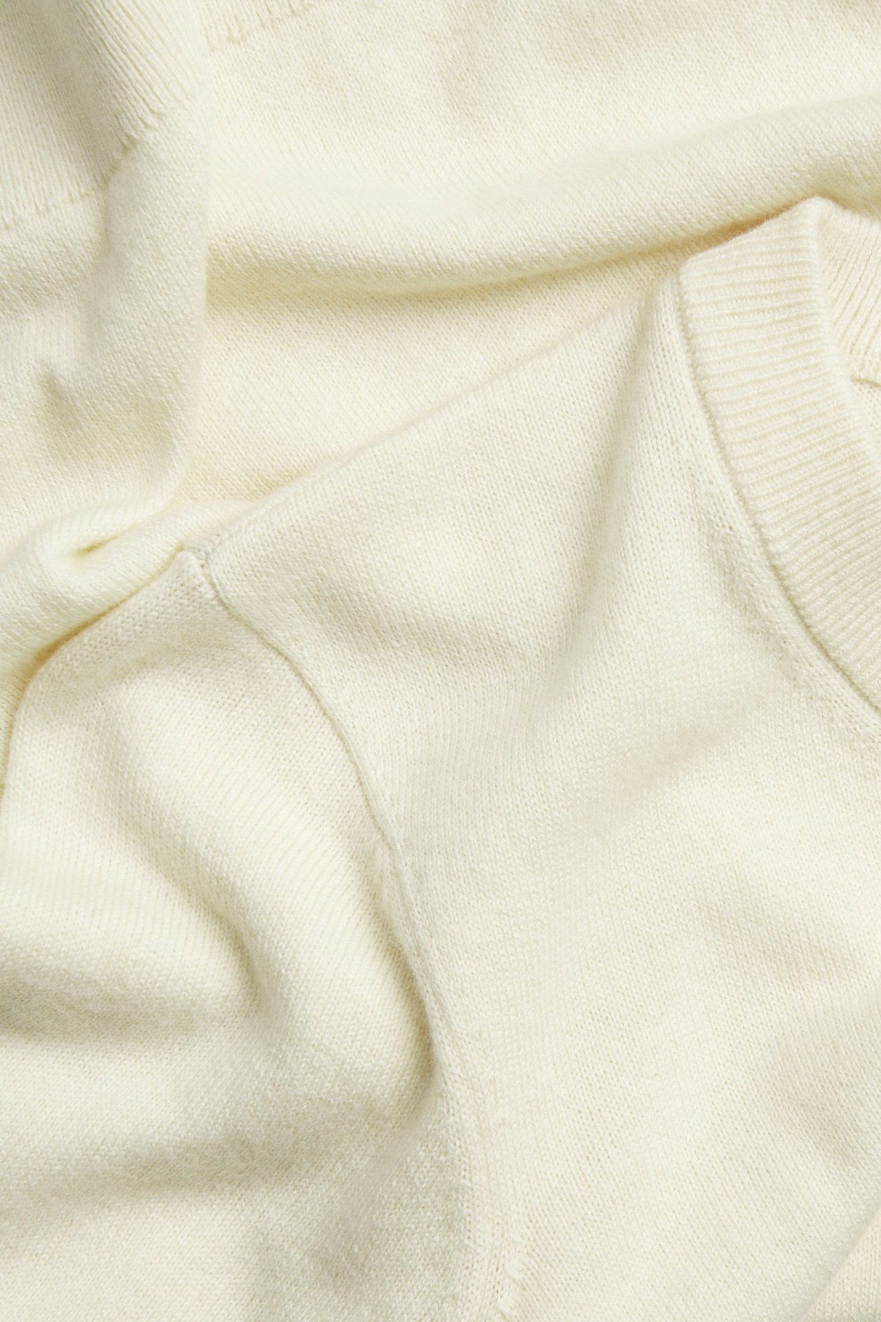 Zbliżenie na ecru, drobno dziergany sweter z krótkim rękawem z domieszką wełny, widoczna faktura.