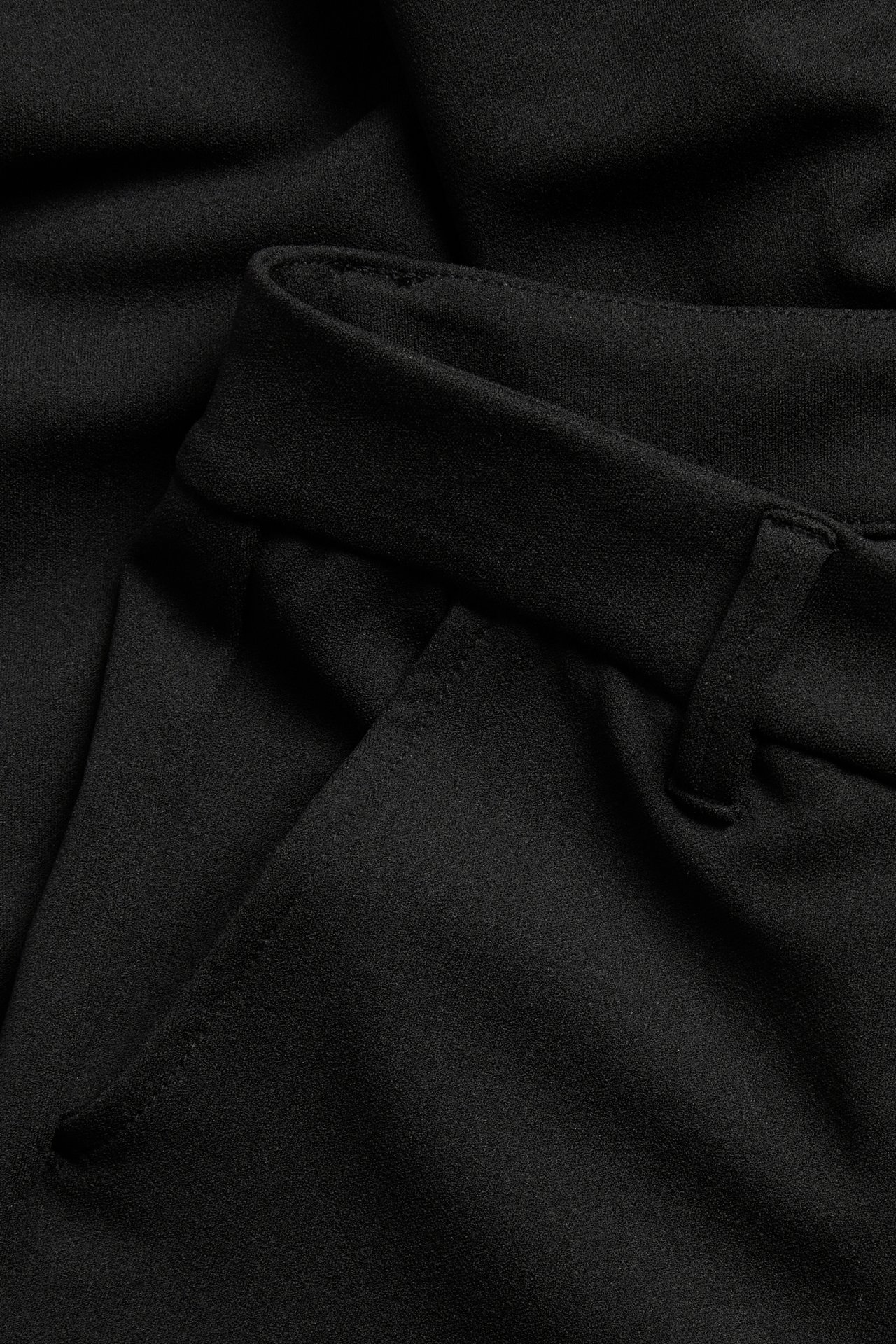 Närmvy av svarta utsvängda trikåbyxor, med ficka och linning med bälteshälla.