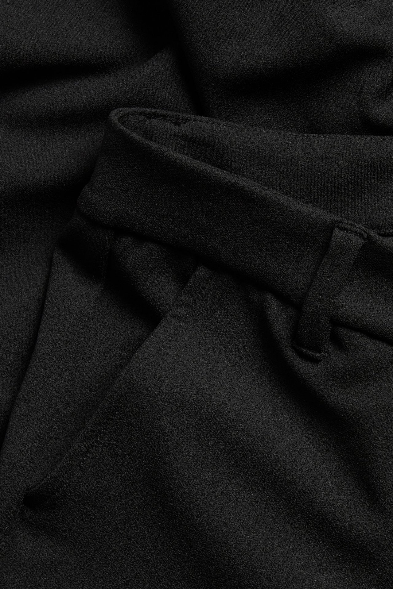 Zbliżenie czarnych dresowych spodni dzwonów, z detalem kieszeni i pasem ze szlufką.