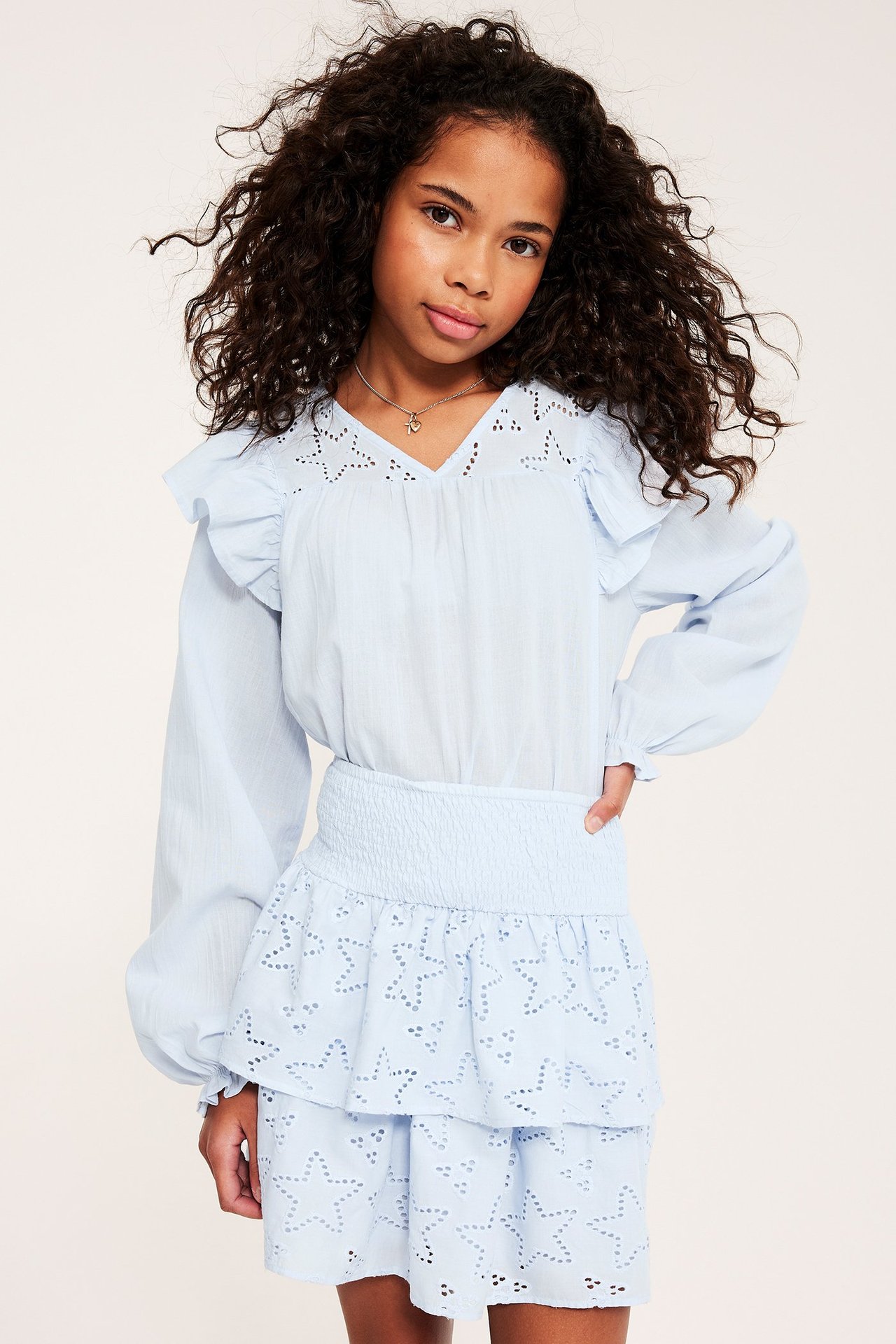 Edestä tytön päällä vaaleansininen puuvillapusero röyhelöillä, tähtikirjonta ja yhteensopiva hame.