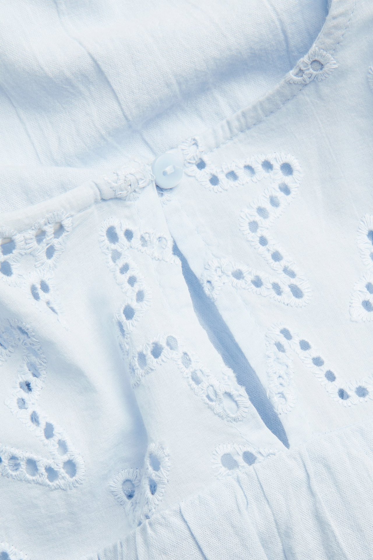 Zbliżenie na jasnoniebieską bluzkę bawełnianą z haftem angielskim i pojedynczym zapięciem na guzik.