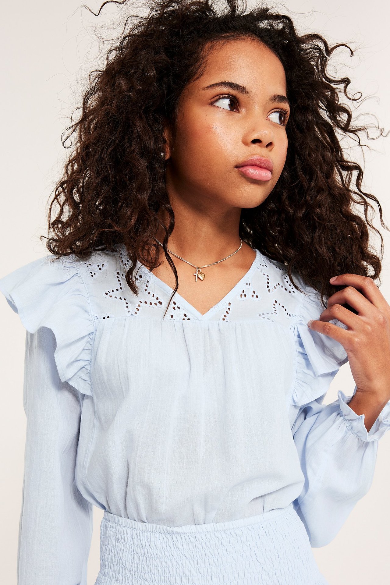 Lähikuva: Lapsityttö vaaleansinisessä puuvillapuserossa, jossa röyhelöitä ja tähtikirjontaa. Resori vyötäröllä, kaulakoru.