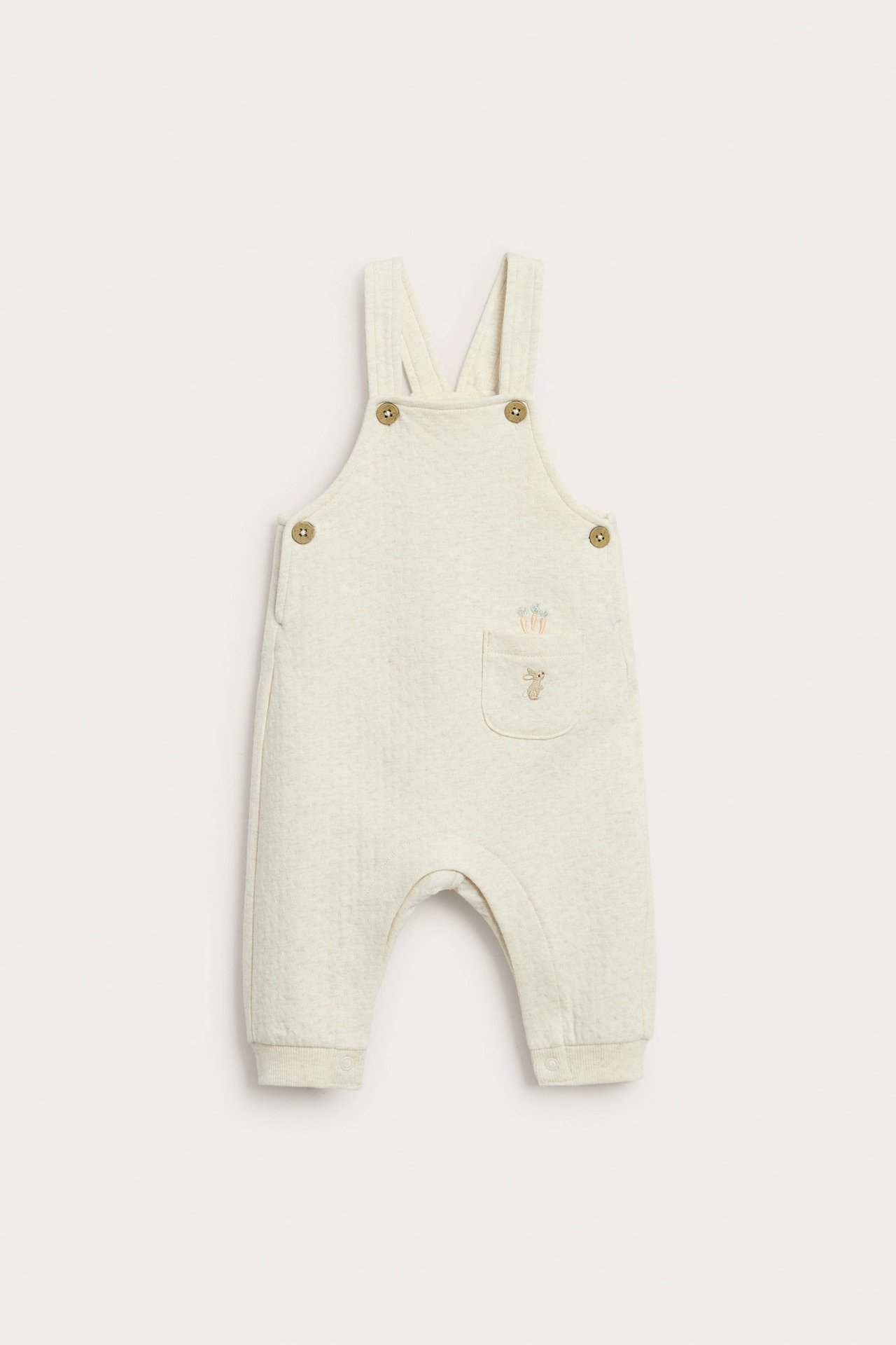 Frontvisning av en beige melange babyjersey-overall med kanin- og gulrotbroderi på en frontlomme.