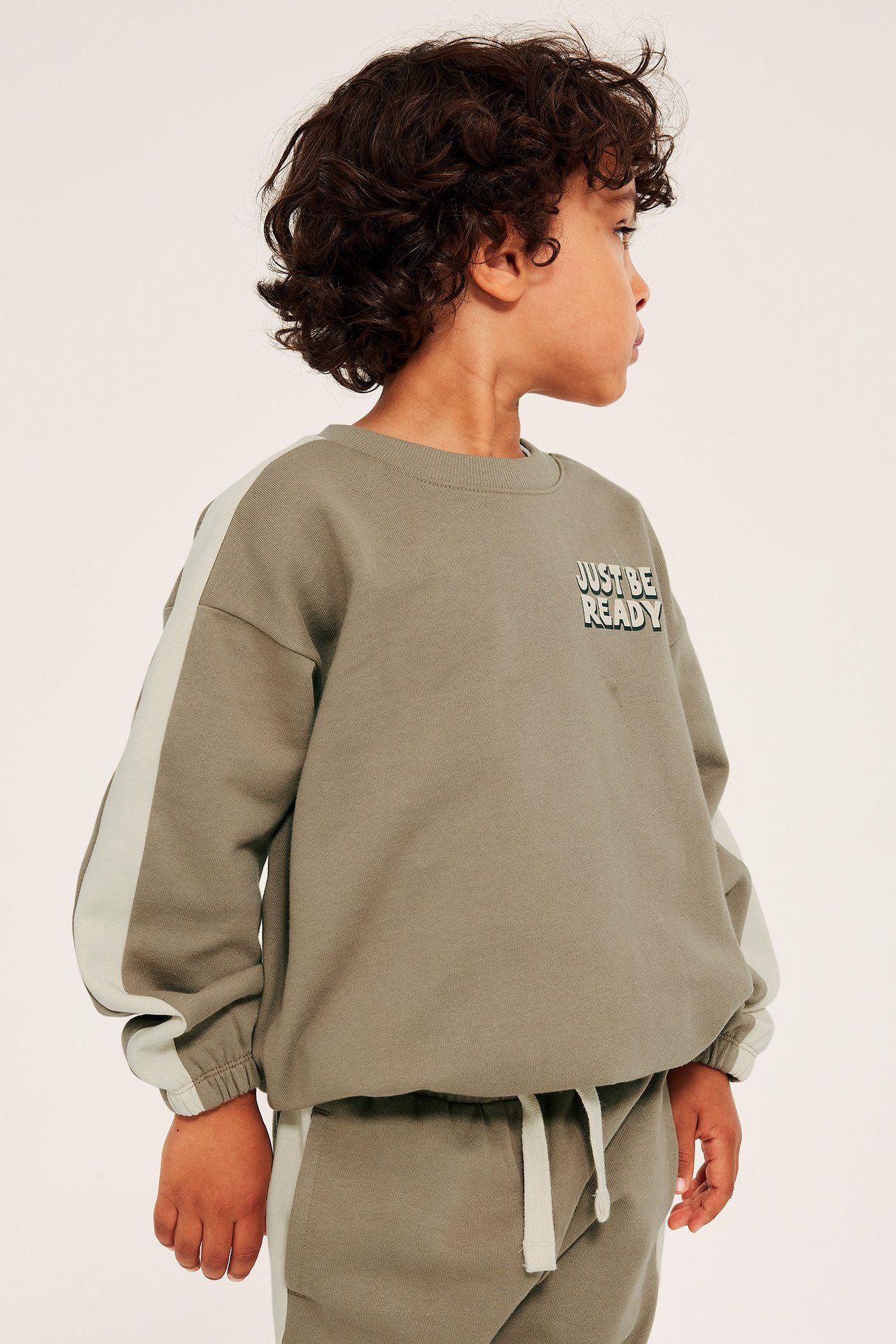 Lapsi beige sweatsh hired kanssa lohkoväri, roikkuva olkapää, kontrastiresori, etukuva.