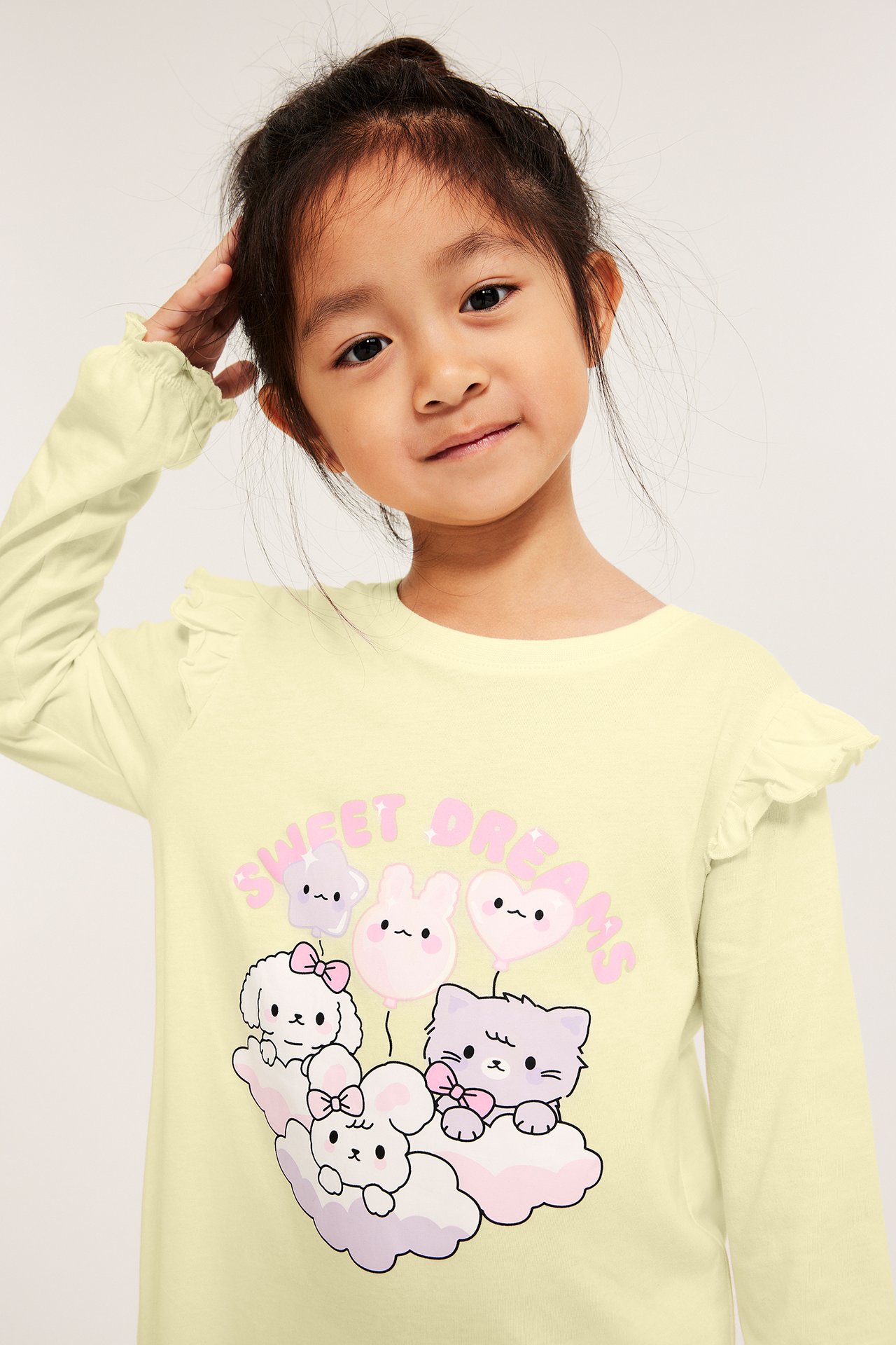 Widok z przodu: dziecko w jasnożółtej bawełnianej koszuli nocnej z długim rękawem, falbankami i nadrukiem.