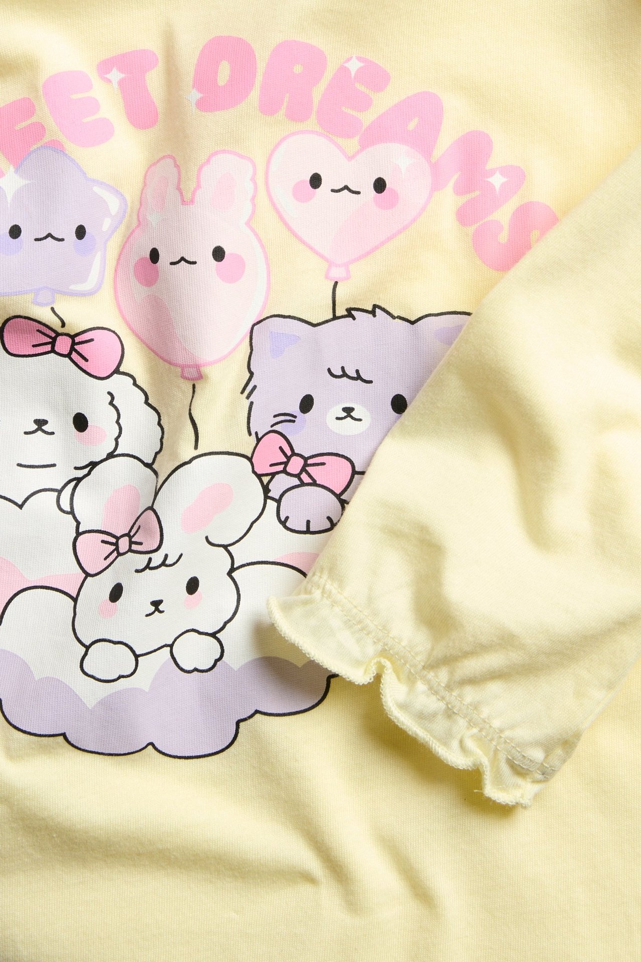 Zbliżenie: jasnożółta, bawełniana koszula nocna dla dzieci z nadrukiem zwierząt "SWEET DREAMS" i falbankami przy mankietach.