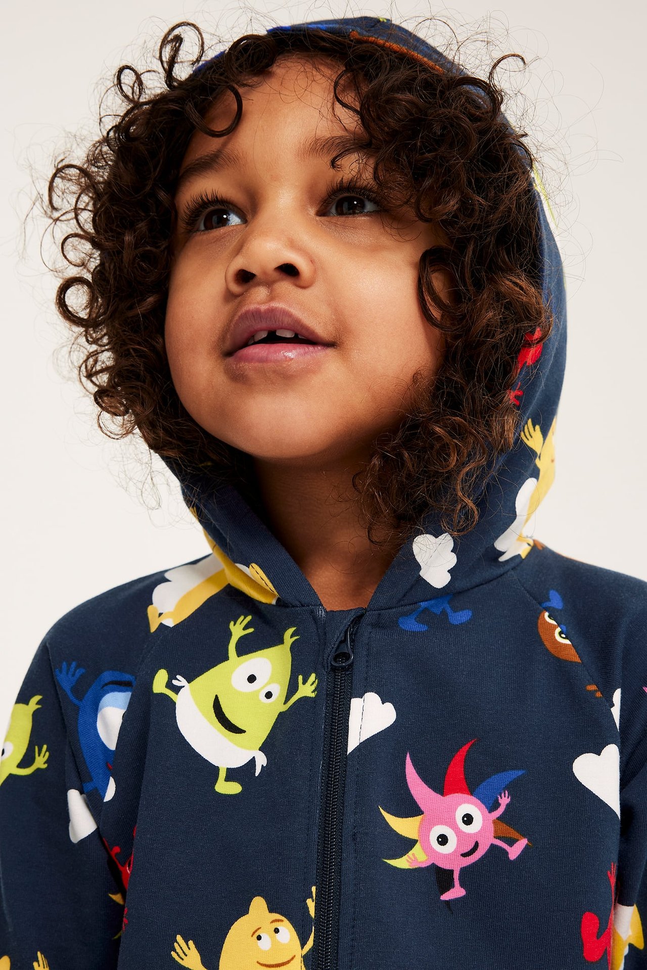 Närbild framifrån på ett barn i en mörkblå mönstrad Babblarna-onesie med huva och dragkedja fram.