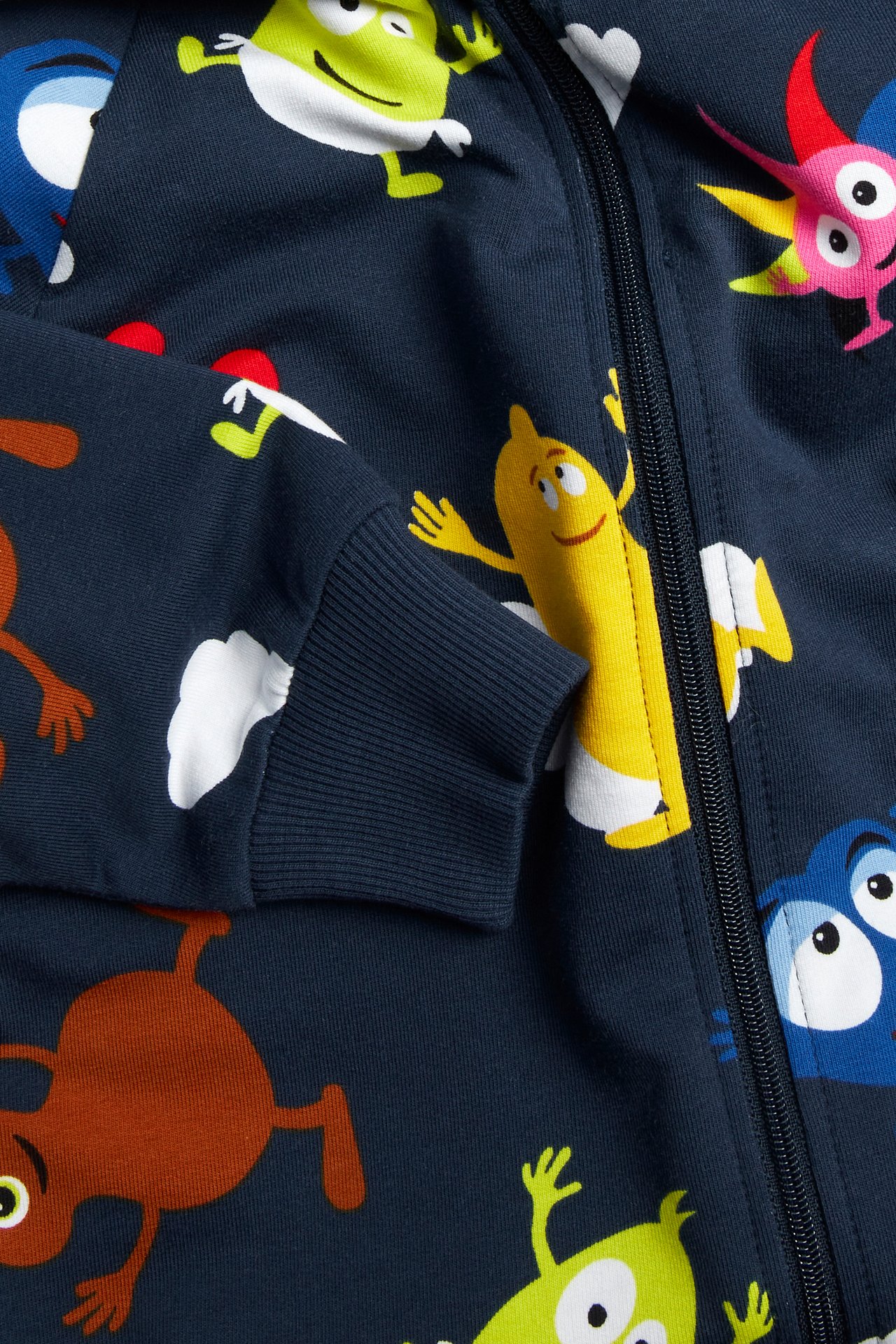 Zbliżenie na granatowy kombinezon niemowlęcy z wzorem Babblarna, zamkiem i ściągaczem na rękawie.