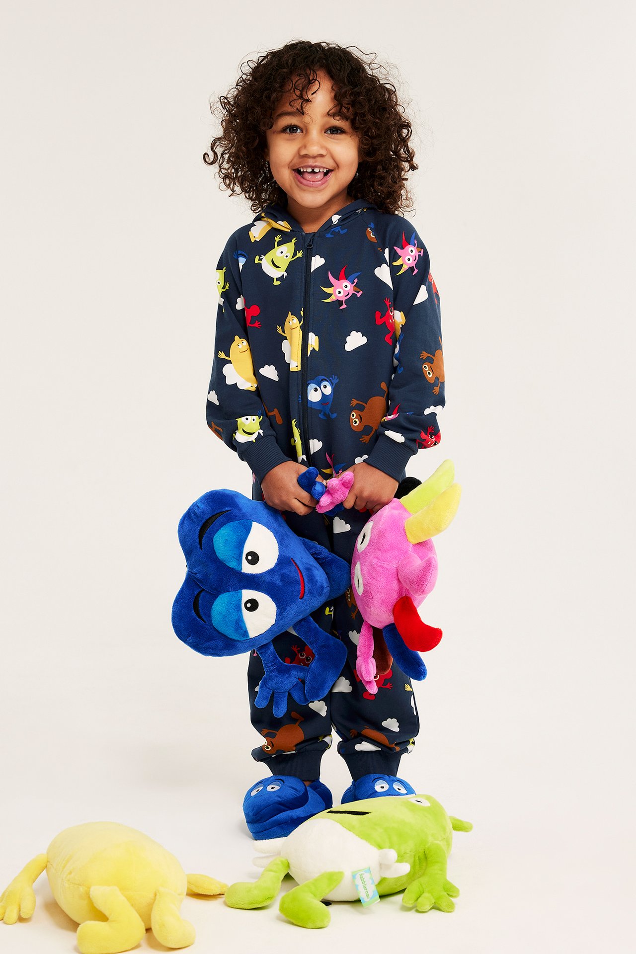 Leende barn i mörkblå Babblarna-mönstrad overall med dragkedja fram, håller två gosedjur.