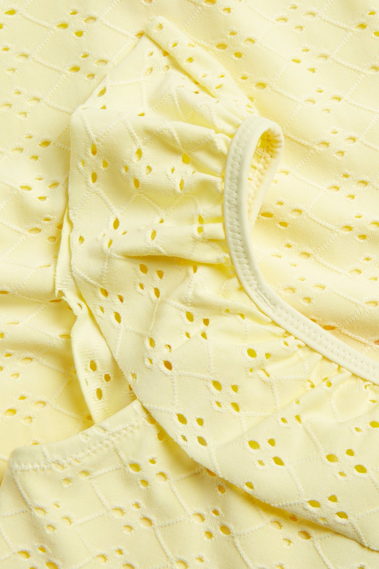 Lähikuva keltaisesta lasten uimapuvusta, jossa broderie anglaise -kuviointi ja röyhelöreuna.