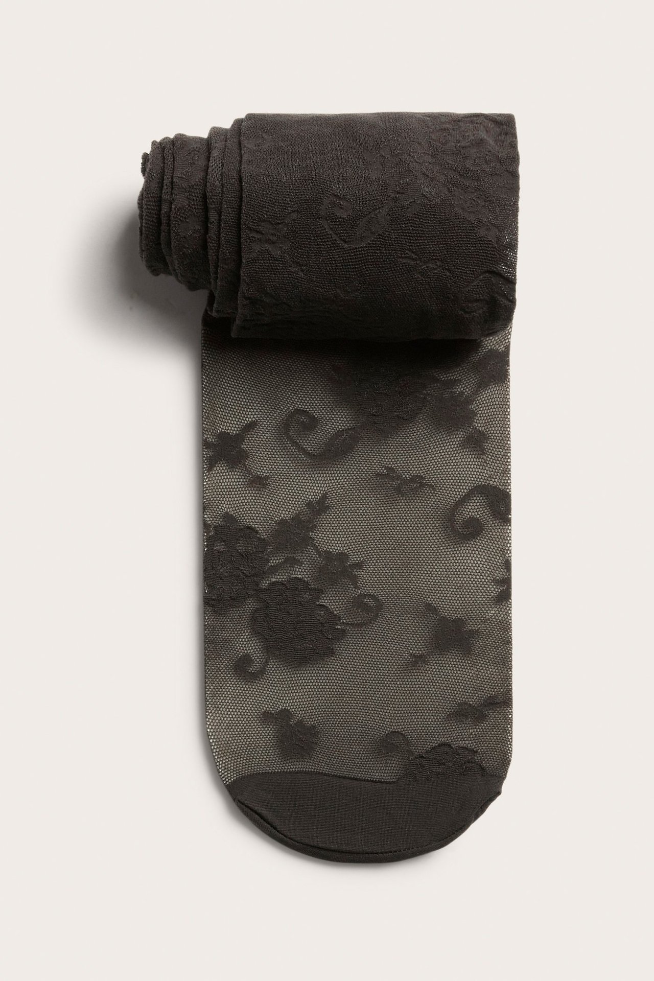 Ylhäältä kuvattu tummanruskeat pitsikuvioiset sukkahousut, osittain rullattuina.