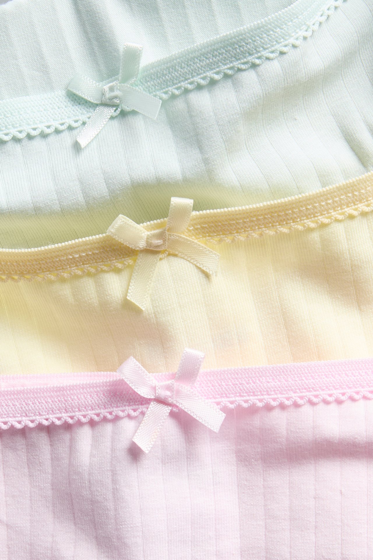 Lähikuva kolmesta ribatusta pikkuhoususta vaaleanpunaisena, keltaisena ja mintunvihreänä, picot-reunoilla ja ruseteilla.